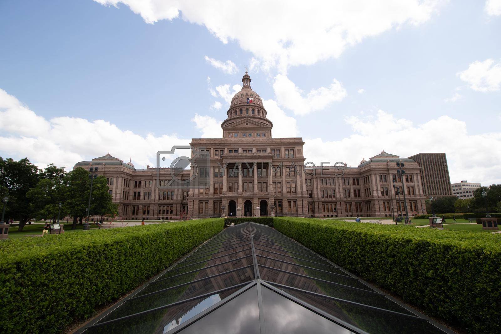 Photo of Texas State Capitol with blue sky and clouds. With green hedges in the back of the Capitol building