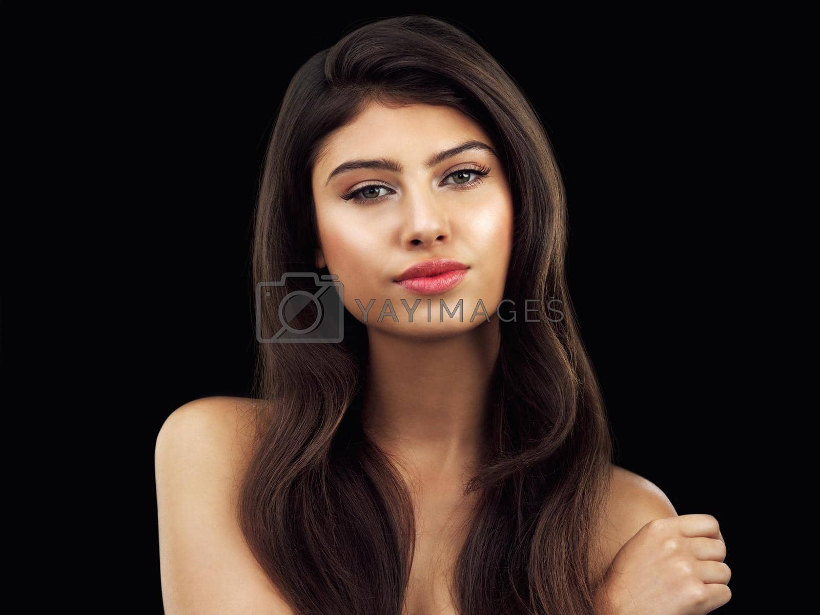 Studio shot of a beautiful woman touching her shoulder posing against a black background.
