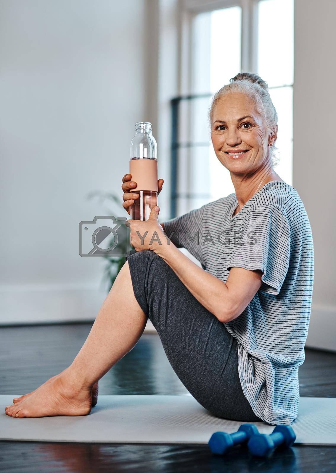 Portrait of a cheerful mature woman practicing yoga while having a drink of water inside of a studio during the day.