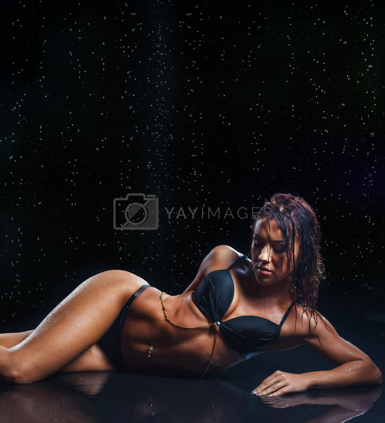 Royalty free image of Sexy brunette fitness woman posing wet over water drops in studio, looking down by fotokvadrat