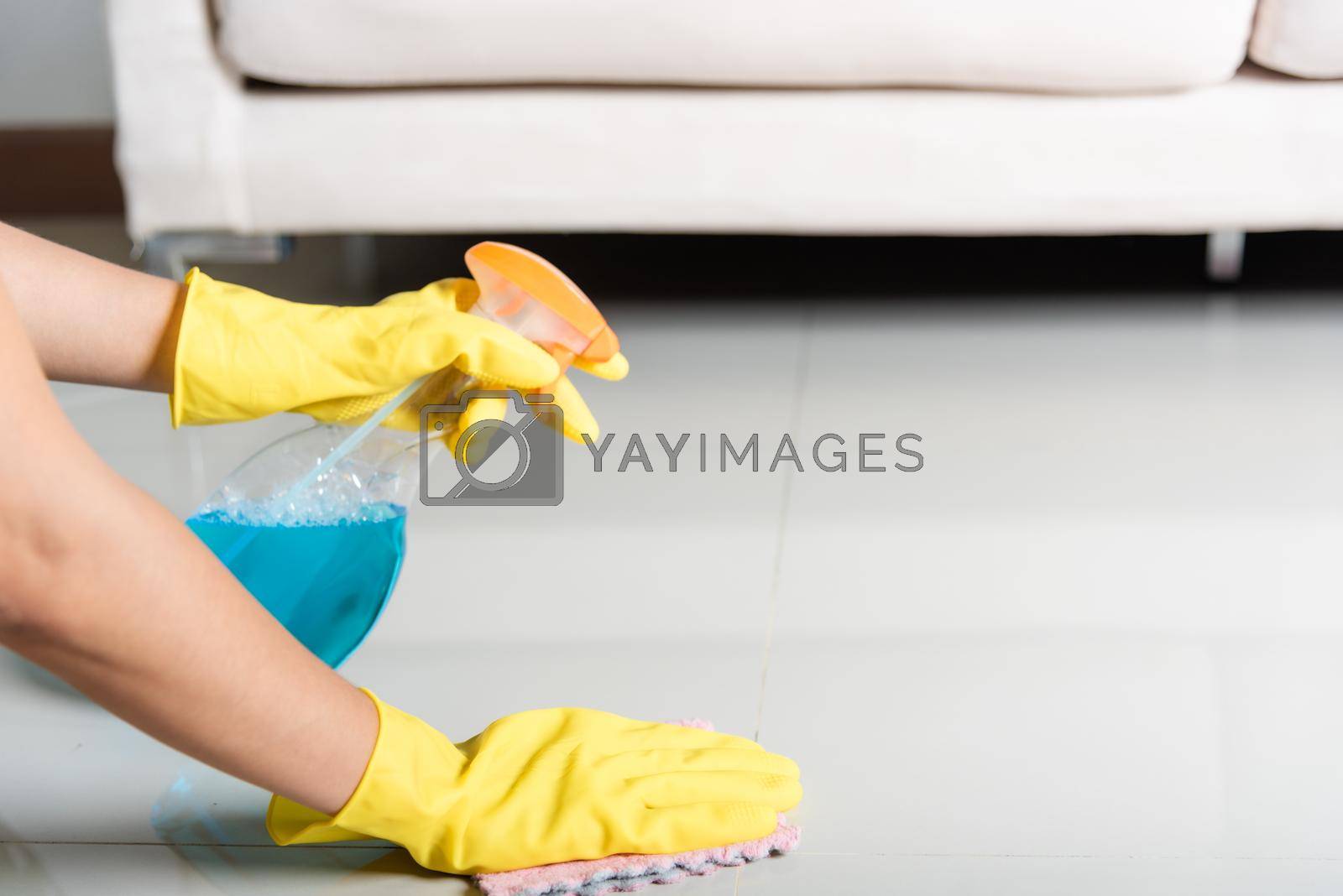 Royalty free image of Asian woman wearing yellow rubber glover with cloth rag and detergent spray cleaning floor at home in living room by Sorapop