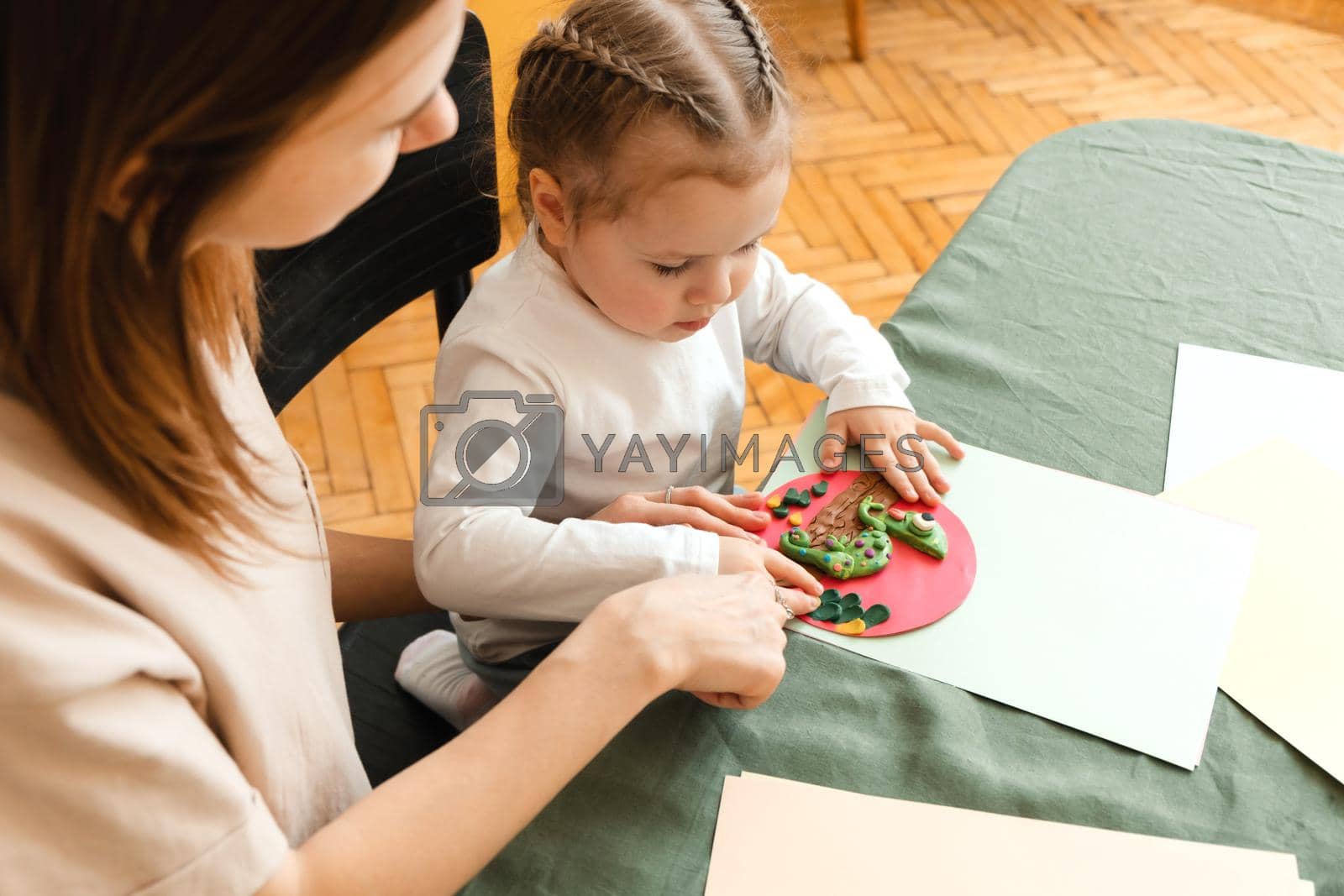 Mother and little daughter enjoy a creative morning by making crafts for kindergarten