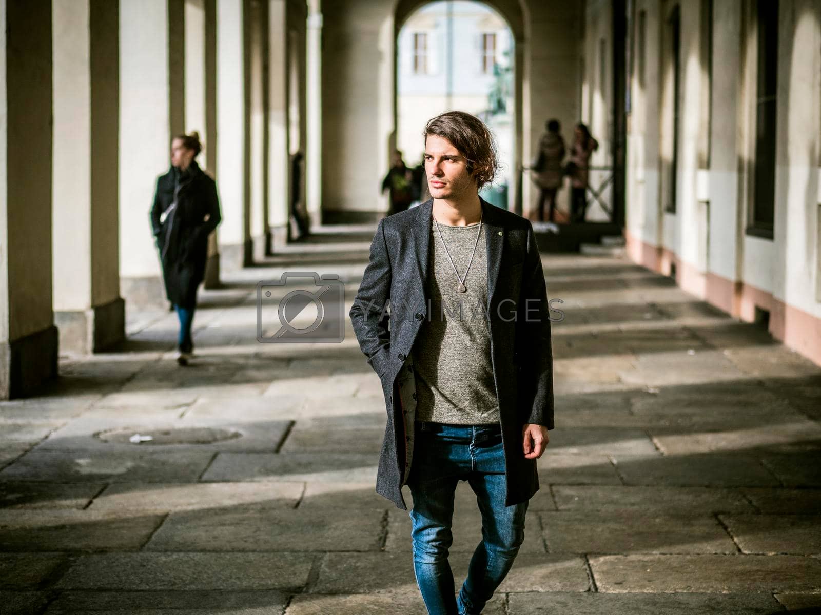 Royalty free image of Elegant young man outdoor wearing wool coat and jeans under colonnade by artofphoto
