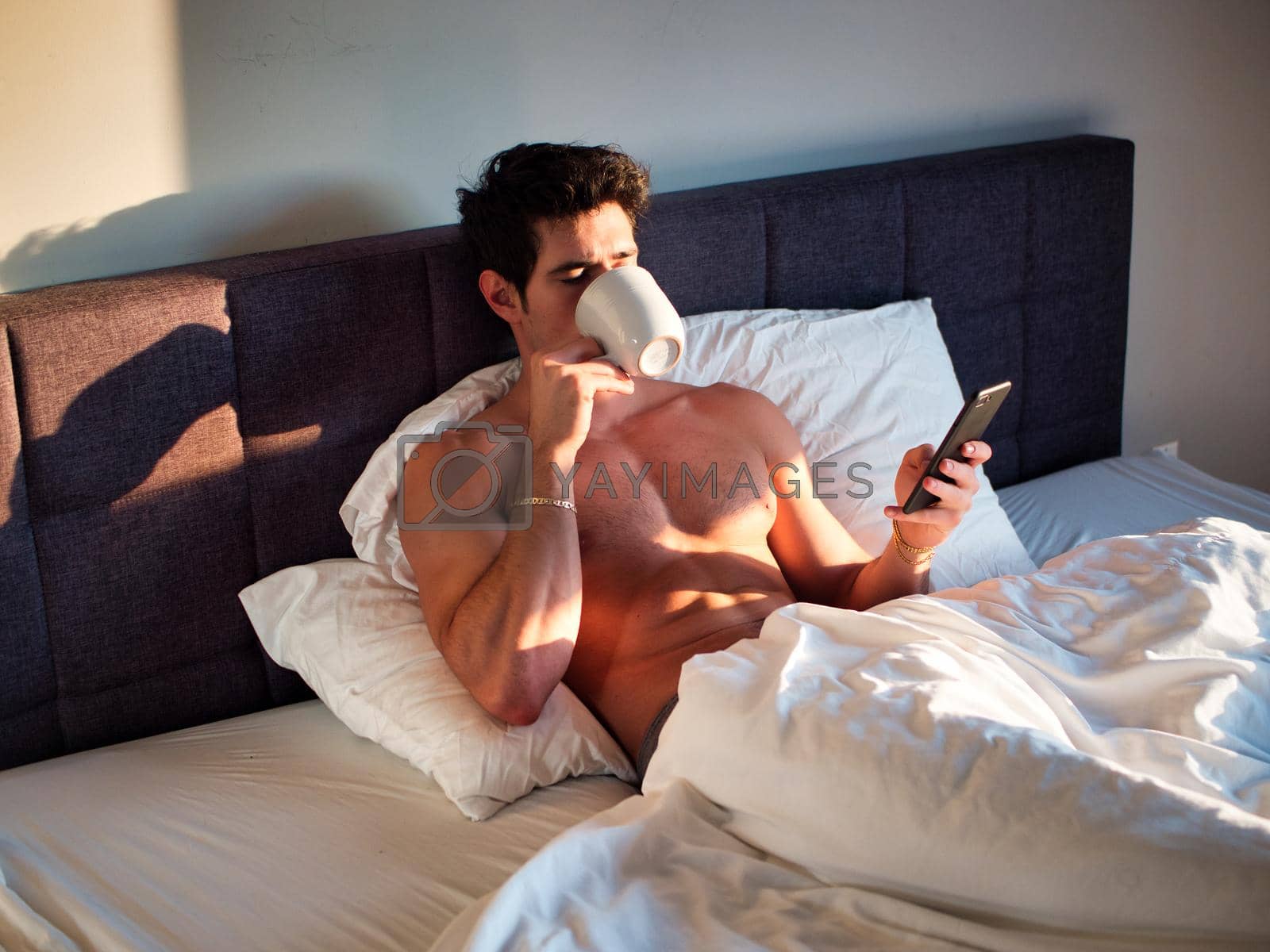 Royalty free image of Naked young man in bed with coffee or tea cup by artofphoto