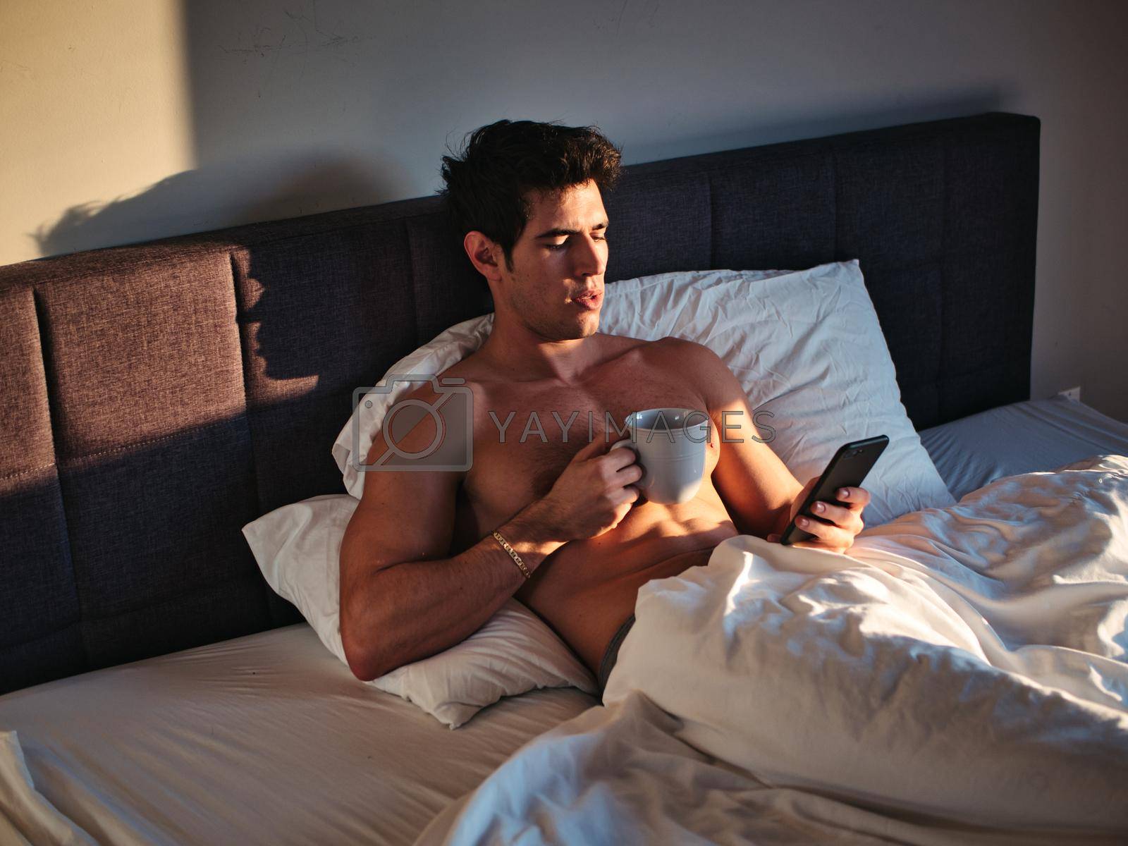 Royalty free image of Naked young man in bed with coffee or tea cup by artofphoto