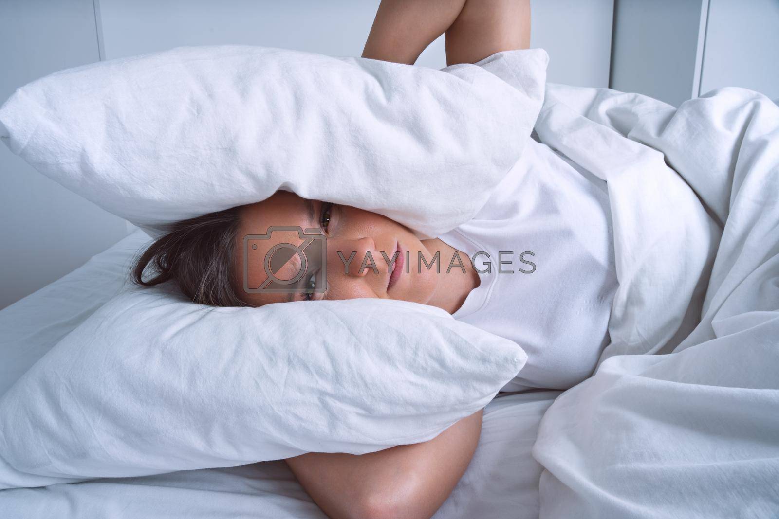 Royalty free image of Young woman can't sleep because of noisy neighbours and covering ears with pillows by DariaKulkova