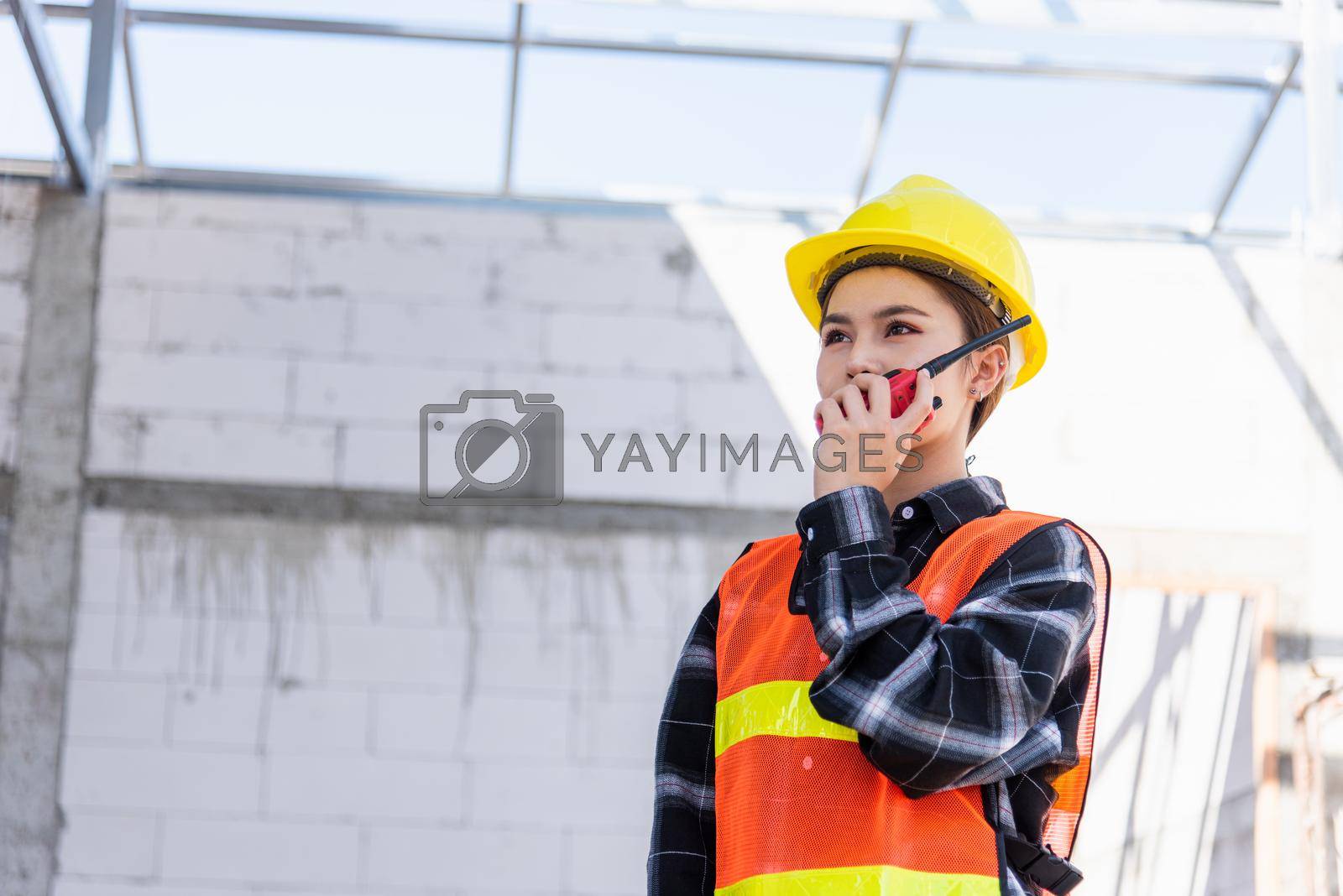 Royalty free image of Asian engineer foreman architect worker woman working at building construction site talking with radio by Sorapop