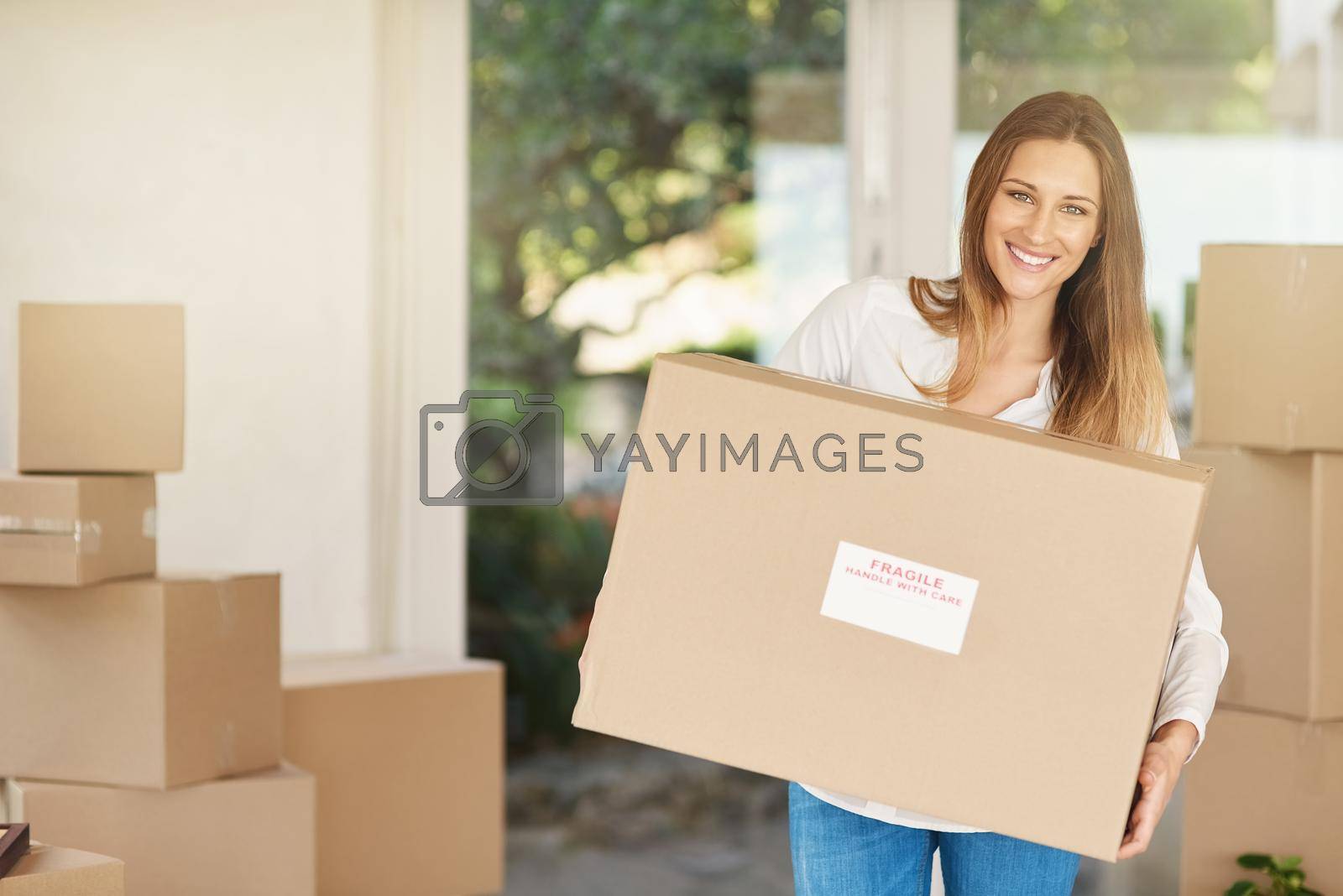 Royalty free image of Heres to a new start. Portrait of a smiling young woman carrying a box on moving into her new house. by YuriArcurs