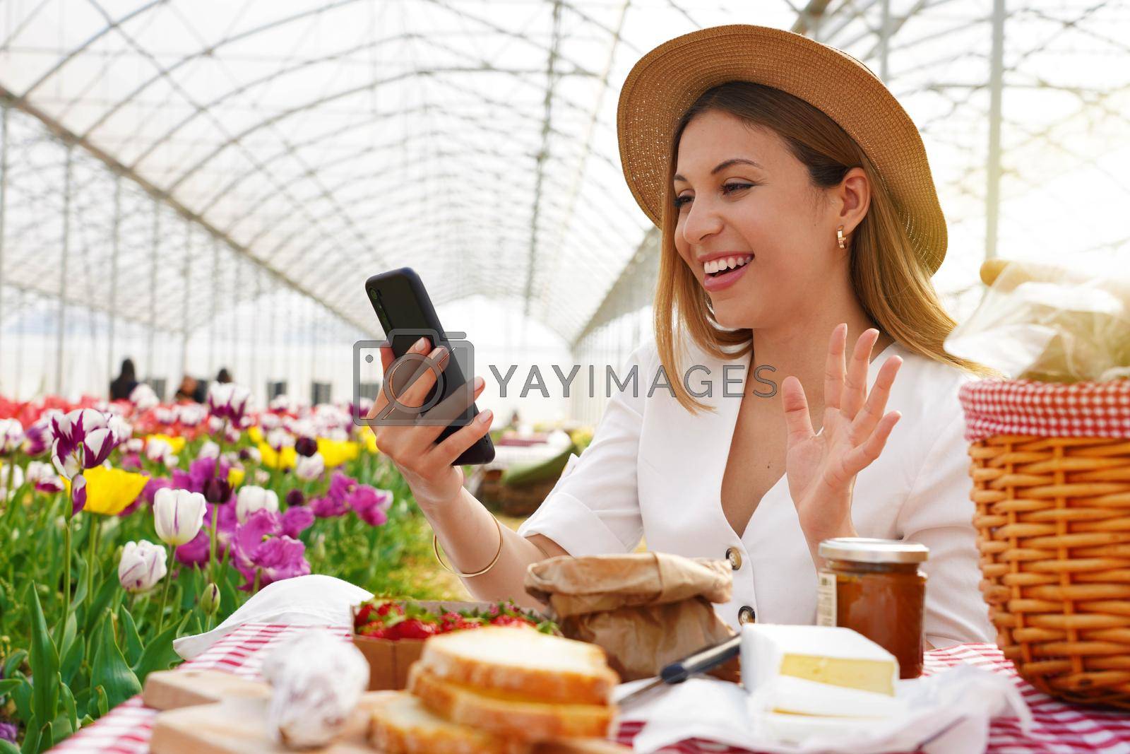 Royalty free image of Influencer doing stories on mobile app about her experience. Young woman video calling with her boyfriend on smartphone while doing picnic on weekend in spring time. by sergio_monti