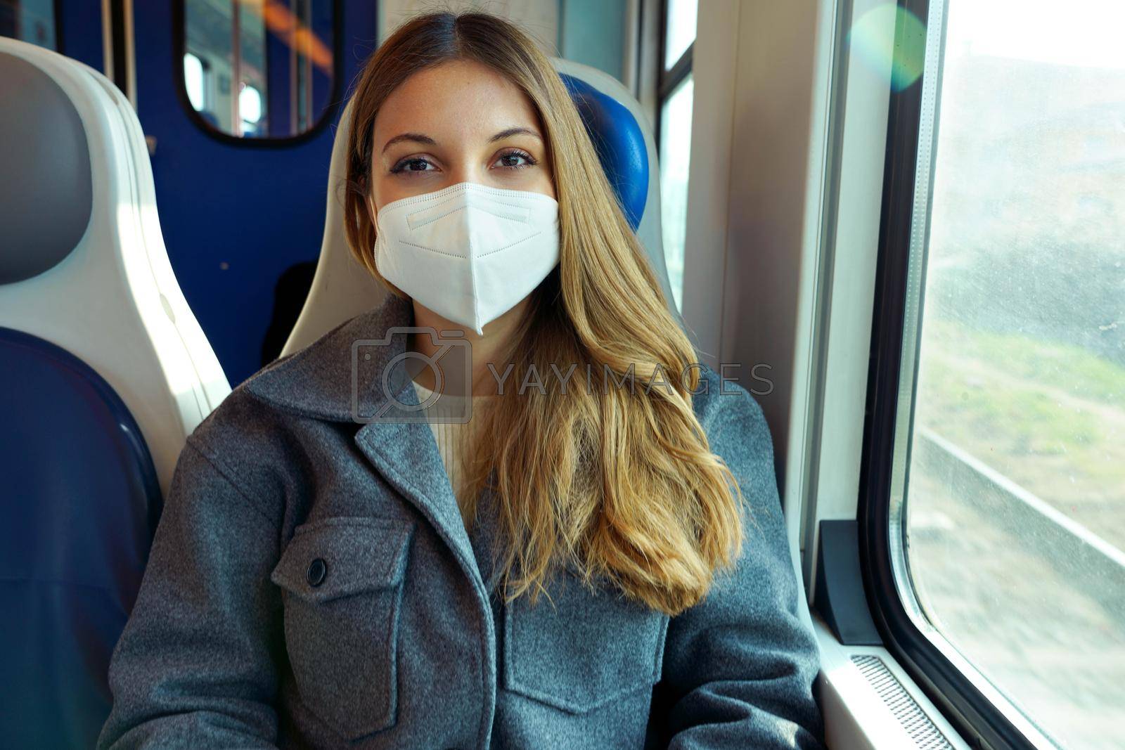 Young woman wearing protective face mask travels on train looking at camera