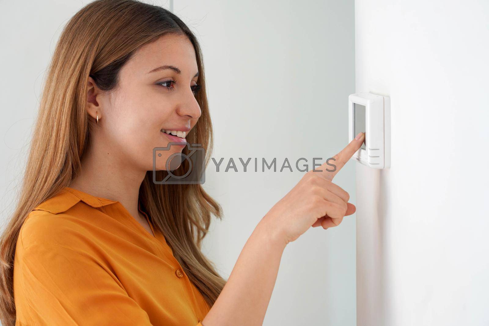 Royalty free image of Portrait of beautiful woman lowering the temperature for energy saving. Woman adjusting digital central heating thermostat at home. by sergio_monti
