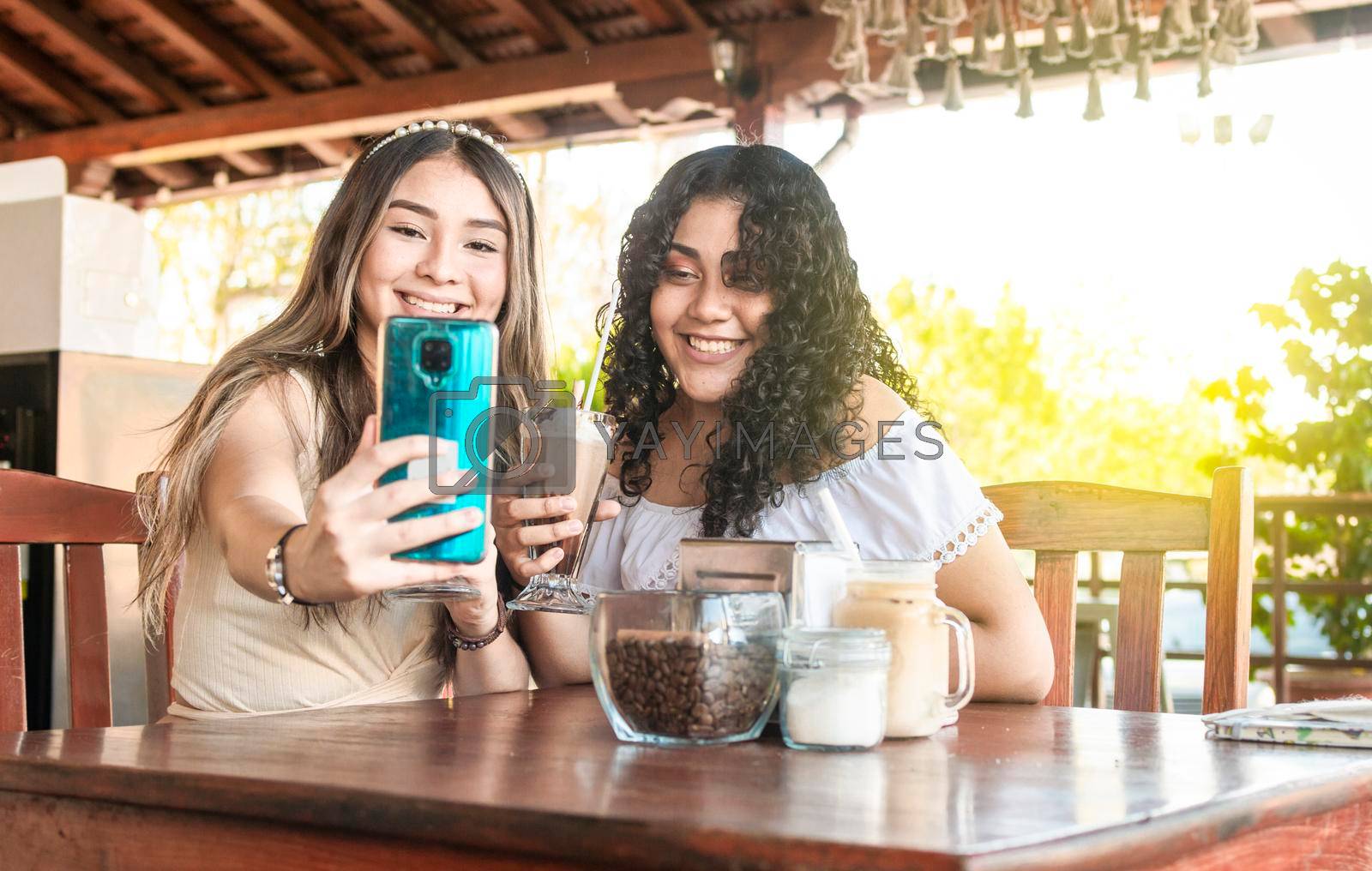 Two girls taking a selfie and drinking coffee, two girls friends in a coffee shop taking a selfie