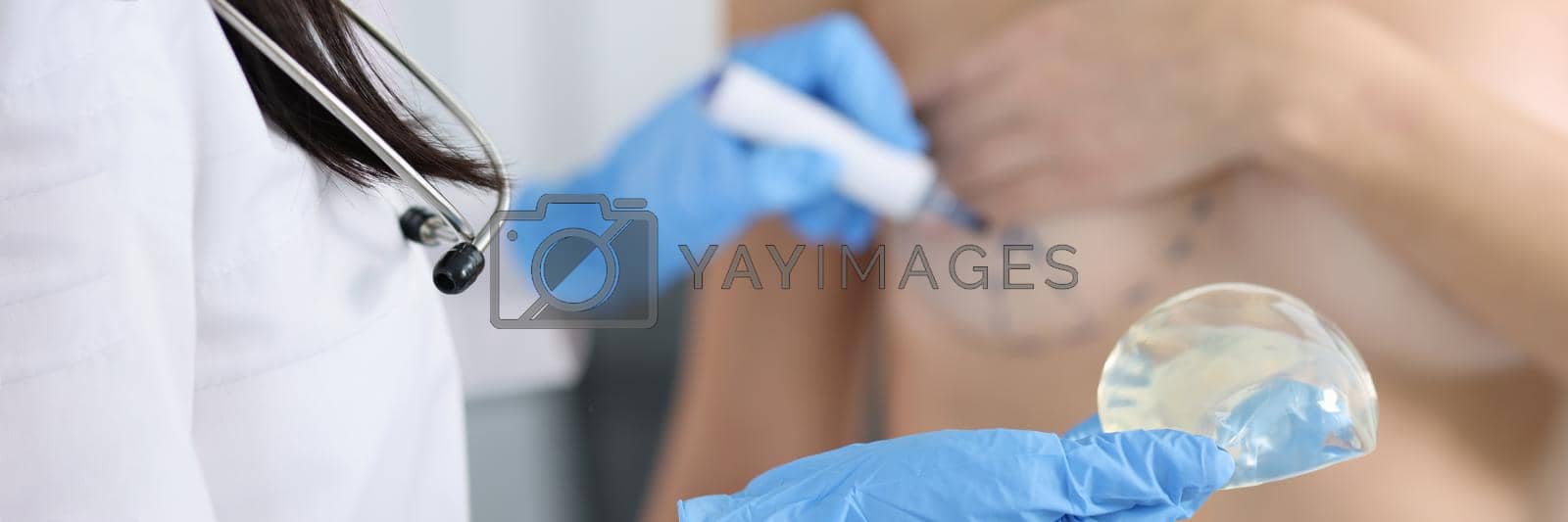 Royalty free image of Plastic surgeon holding silicone breast implant and applying preoperative markings to patient chest closeup by kuprevich