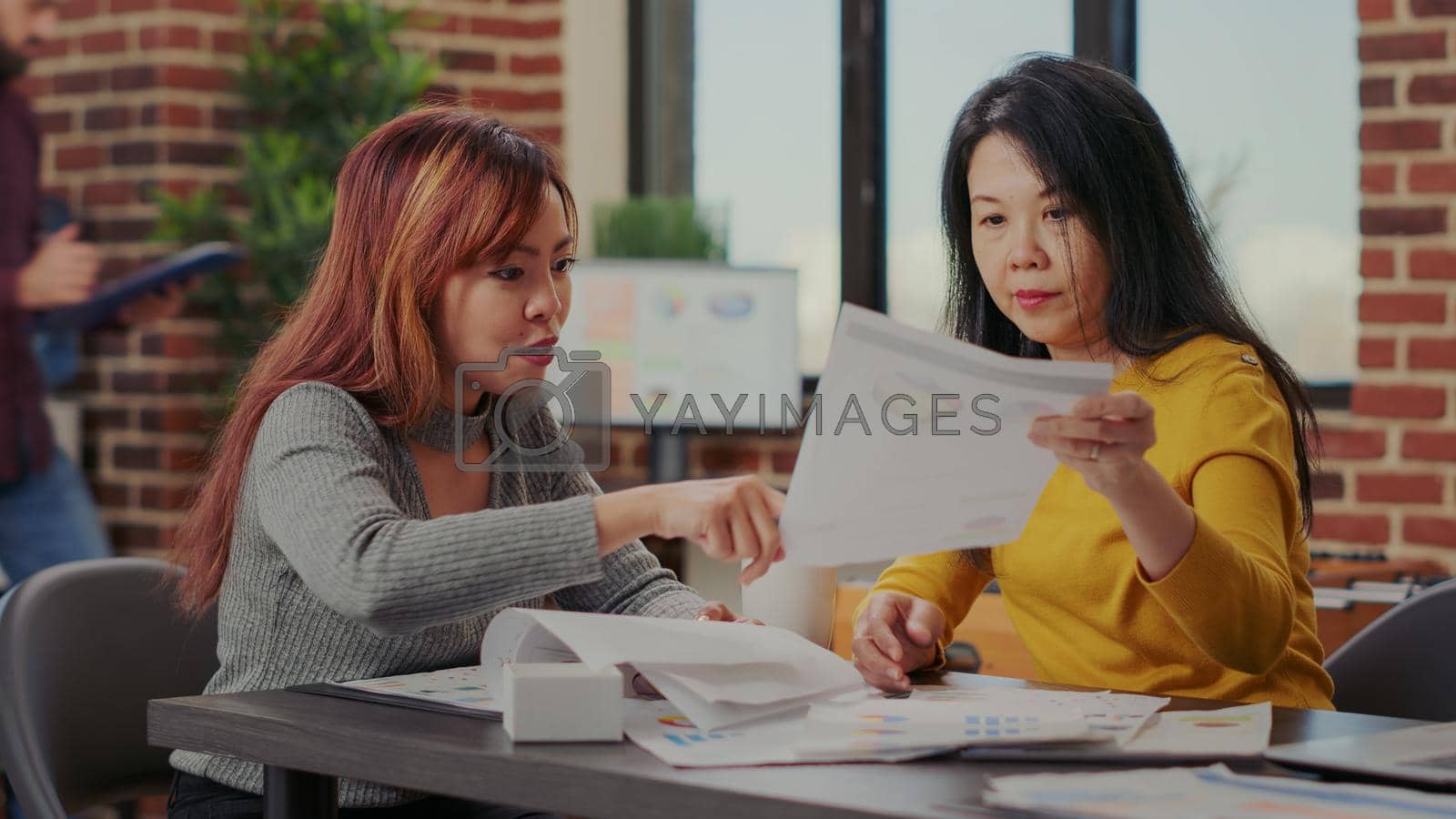 Business partners working with e commerce statistics in office. Team of asian women analyzing financial graphs to develop sales growth and marketing presentation. Workers briefing ideas
