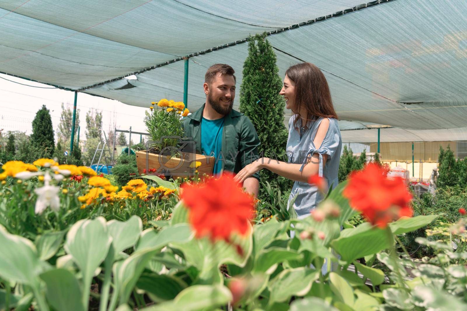 Royalty free image of Worker helping female customer to buy flowers in garden center by Mariakray
