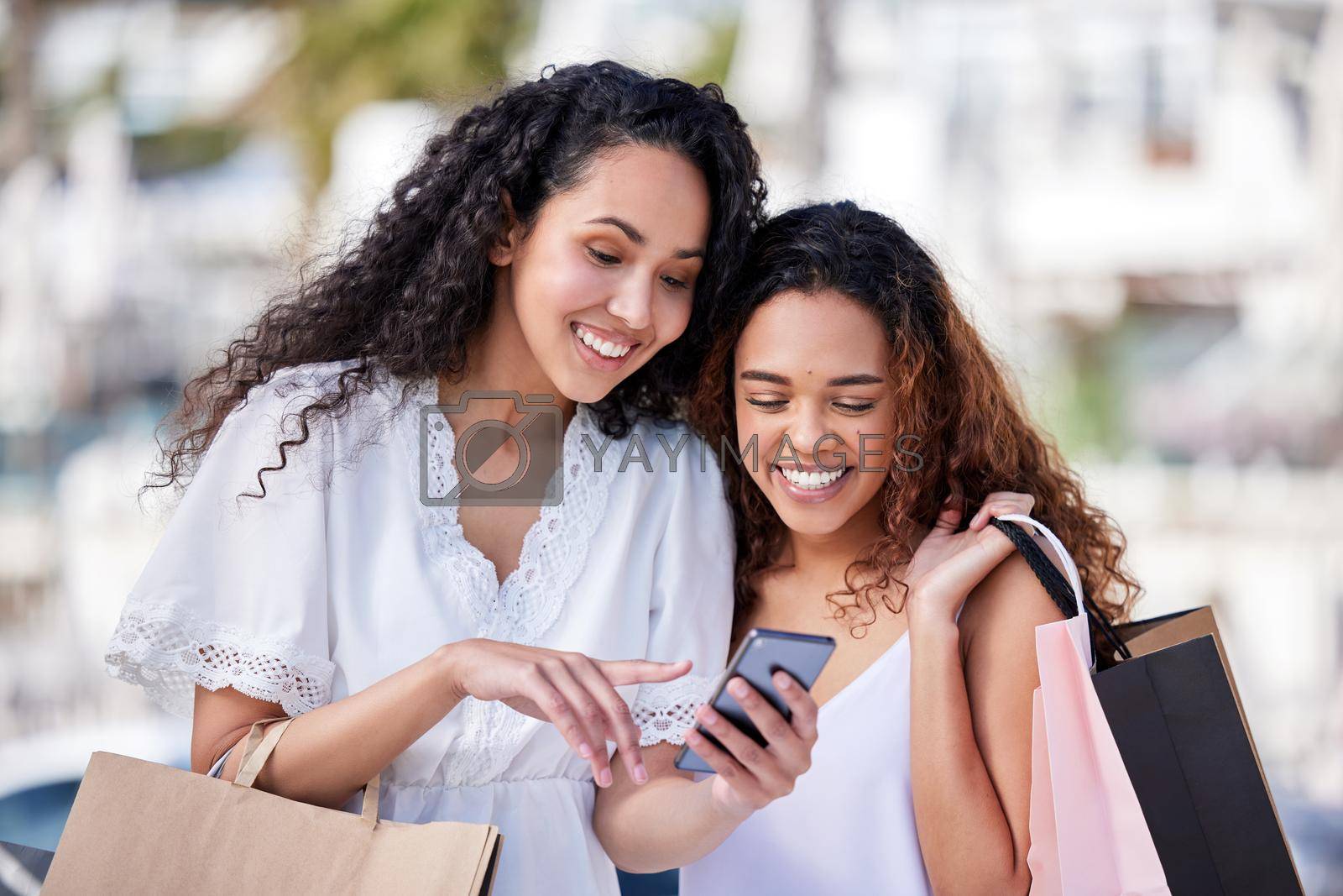 Shot of two young women using a smartphone while shopping against an urban background.