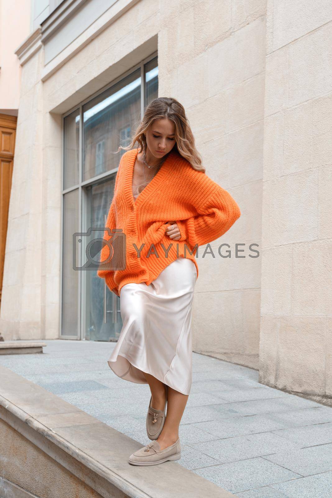 Royalty free image of Portrait of fashionable women in orange sweater and beige dress posing in the street by Ashtray25