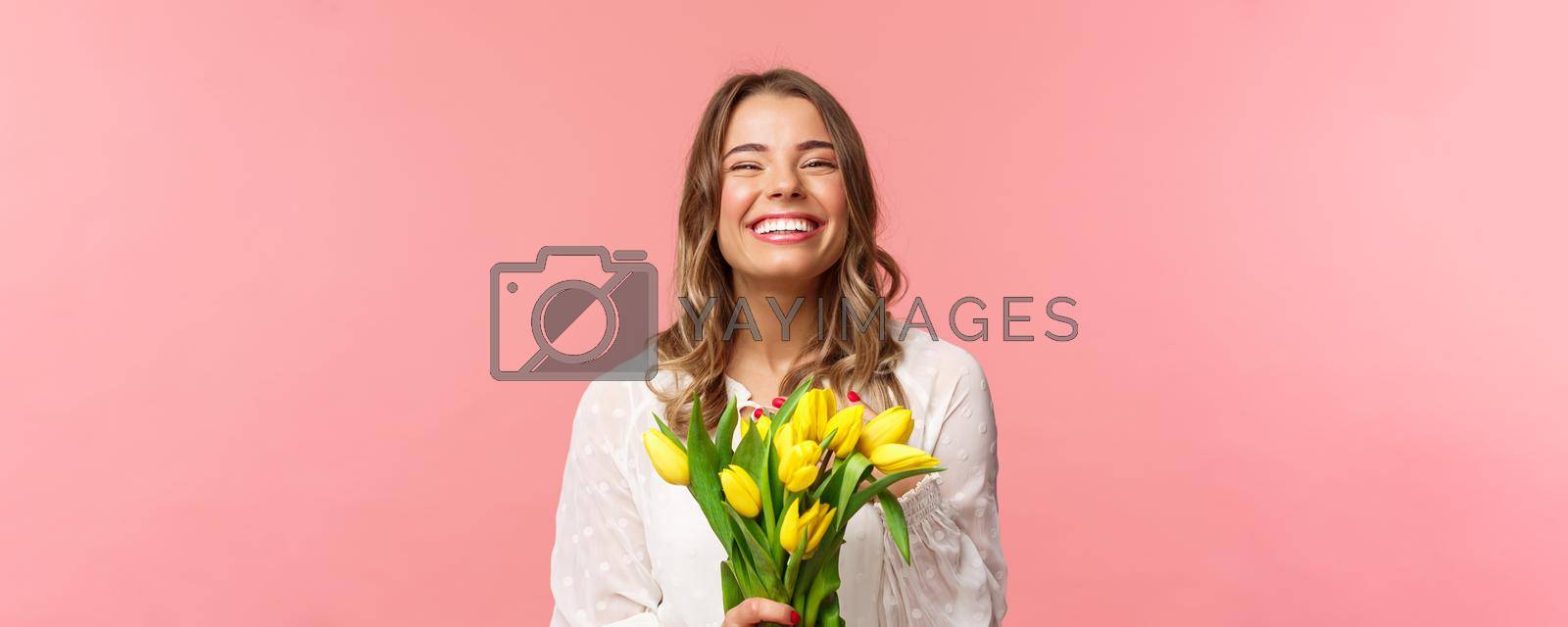 Spring, happiness and celebration concept. Close-up of happy and carefree blond european girl receive beautiful bouquet of flowers, holding yellow tulips, smiling and laughing, pink background.