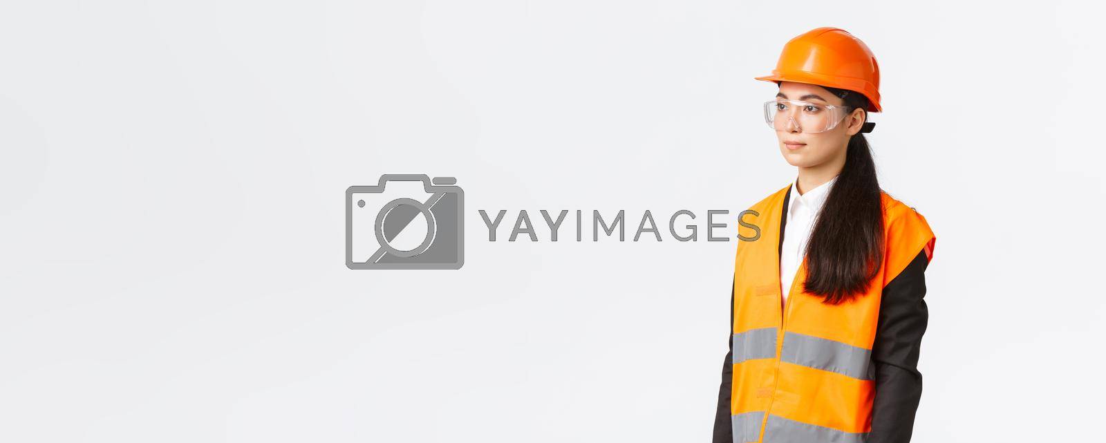Royalty free image of Profile of serious asian female businesswoman inspecting construction area, chief engineer looking left, wearing safety helmet and reflective clothing, standing white background by Benzoix