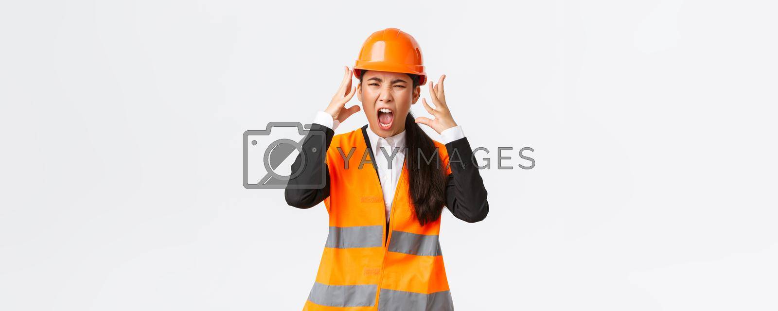 Royalty free image of Mad and outraged asian female chief engineer, construction manager burst in rage, losing temper at employees, shouting and shaking hands aggressive, scream furious as scolding someone by Benzoix