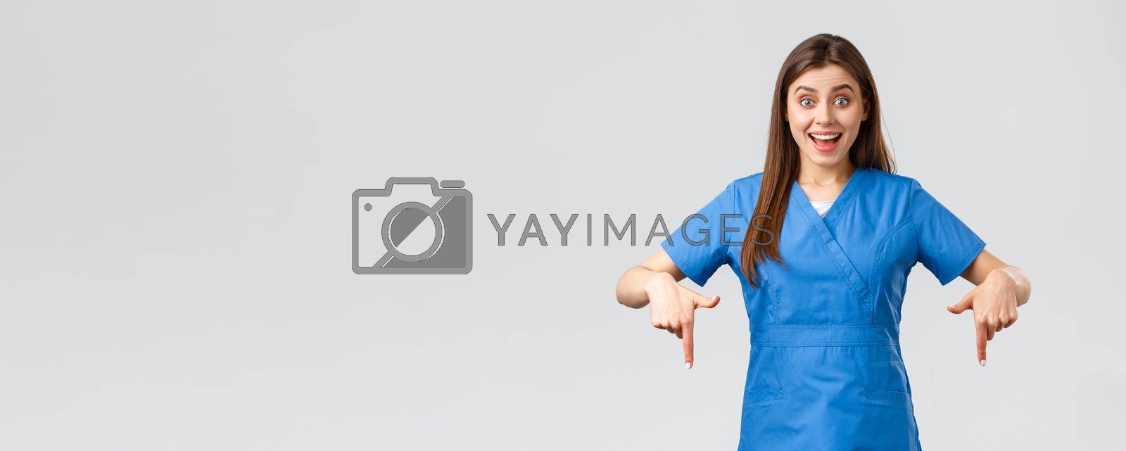 Healthcare workers, prevent virus, covid-19 test screening, medicine concept. Excited happy attractive nurse or doctor in blue scrubs, pointing fingers down, found great promo, showing banner.