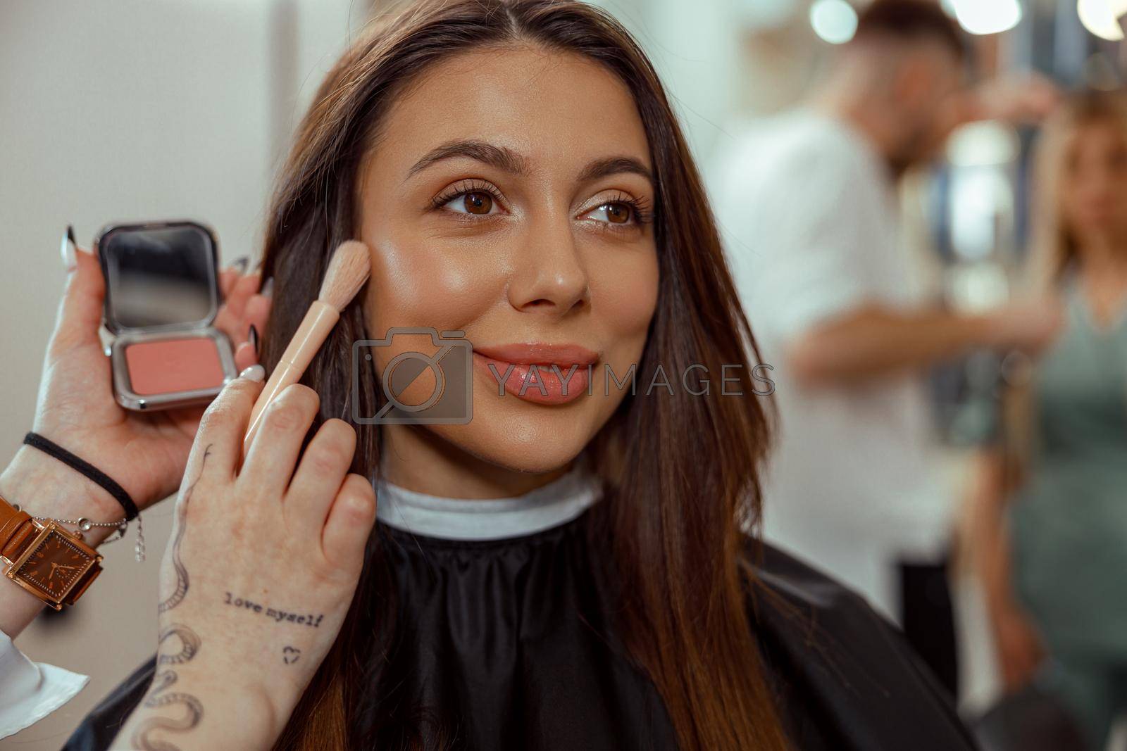 Portrait of smiling woman getting makeup with a brush in beauty salon. Beauty salon services