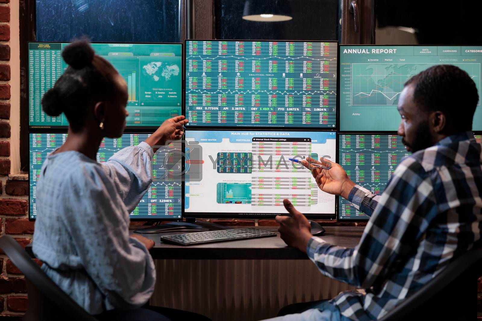 African american financial advisors reviewing real time market data and statistics in order to sell stocks. Hedge fund traders sitting at workstation while pointing at display with live index charts.