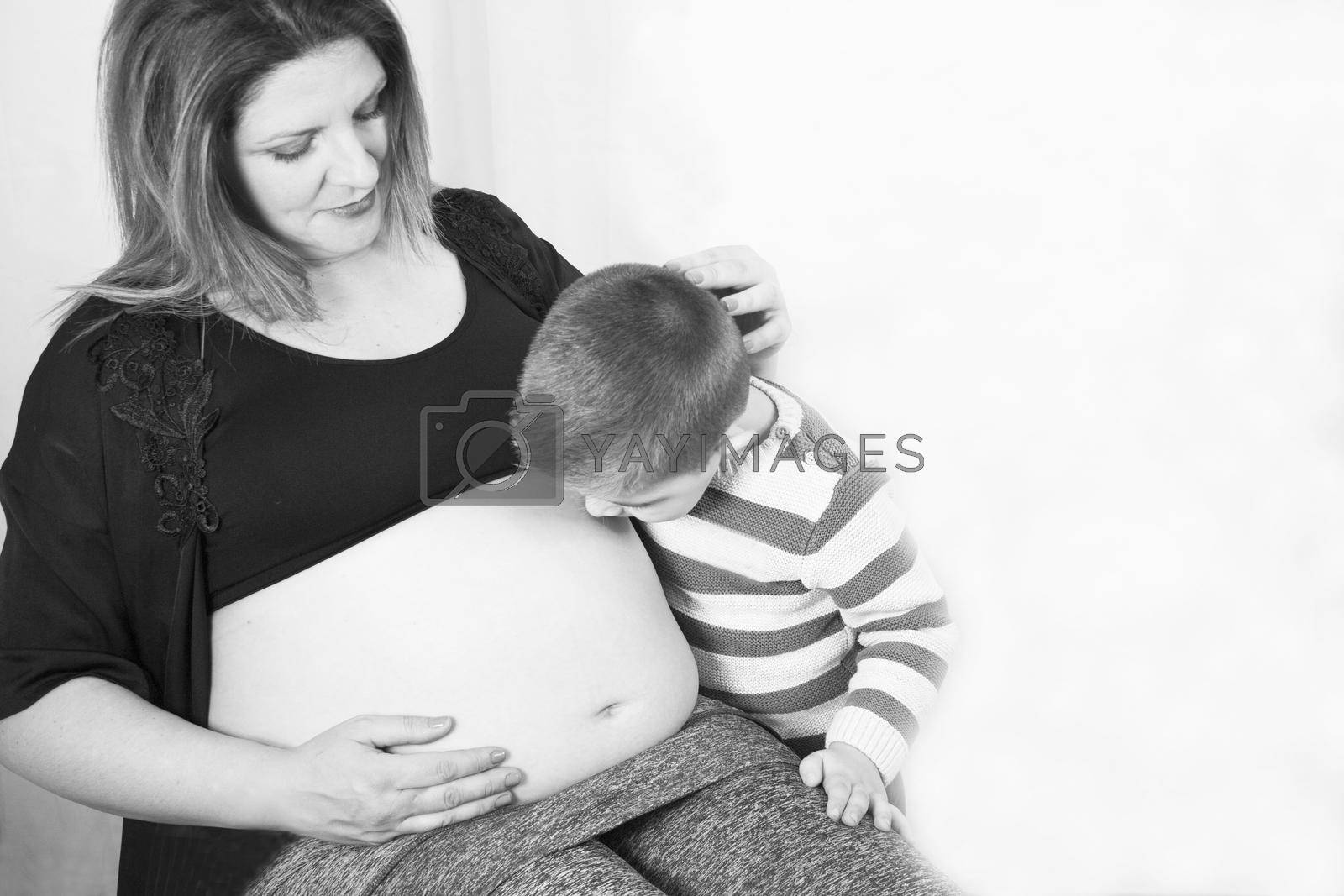 Eight month pregnant woman and three year old son kissing belly. Smiling