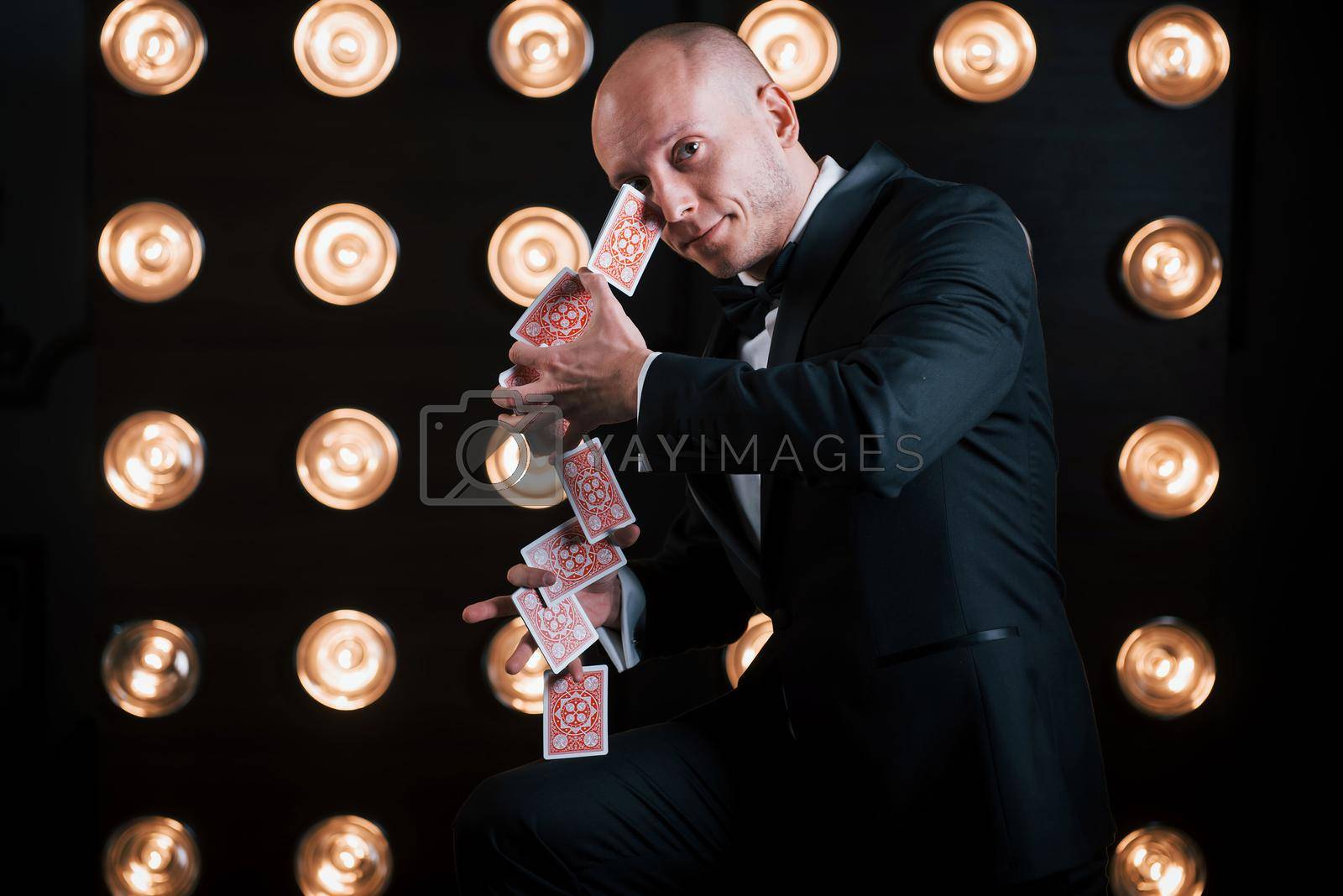 Royalty free image of These cards is like he's second nature. Magician in black suit standing in the room with special lighting at backstage by Standret