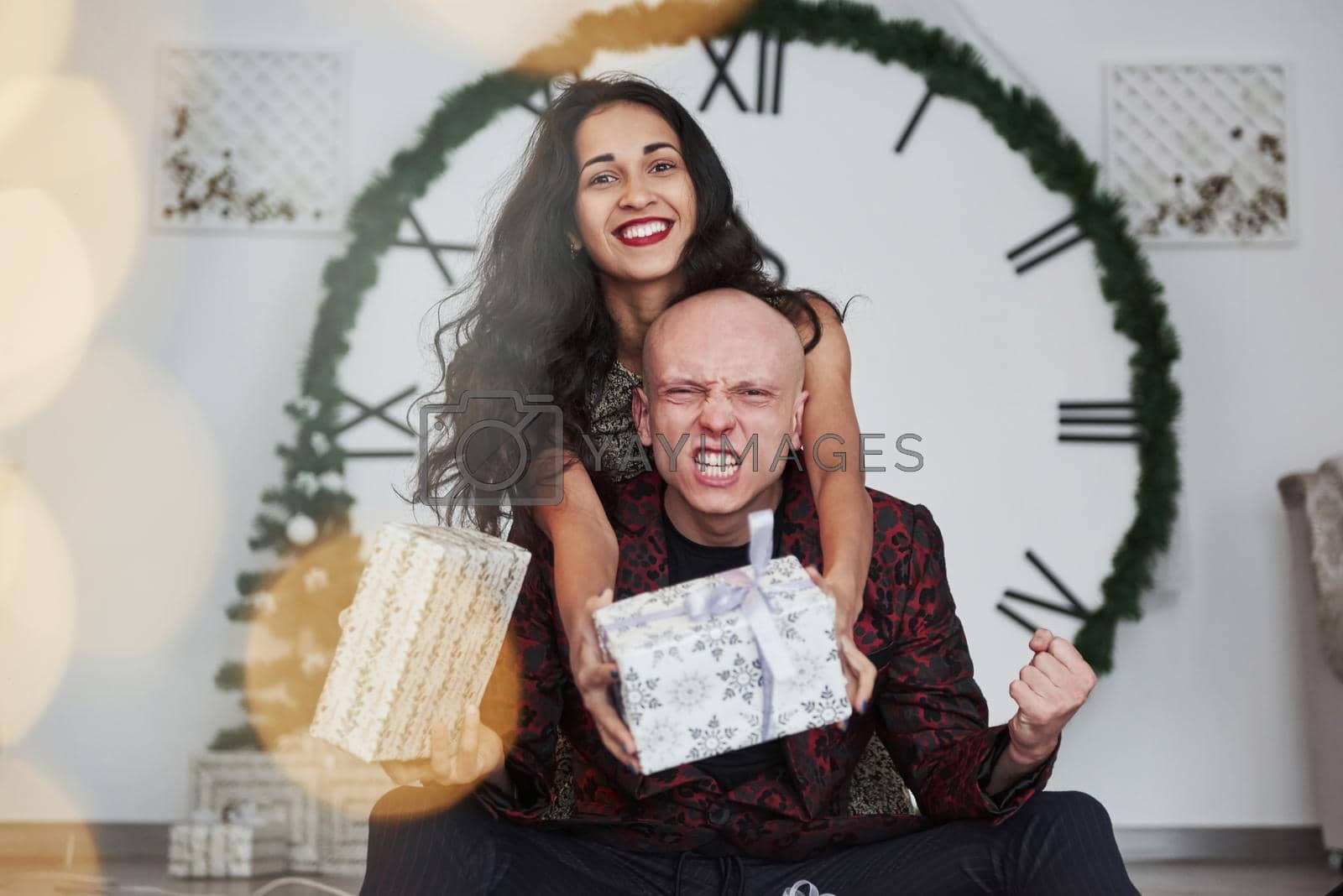 Royalty free image of Guy finally gets his gift. Couple in the holiday clothes. Big watch at background. Five minutes to New year by Standret