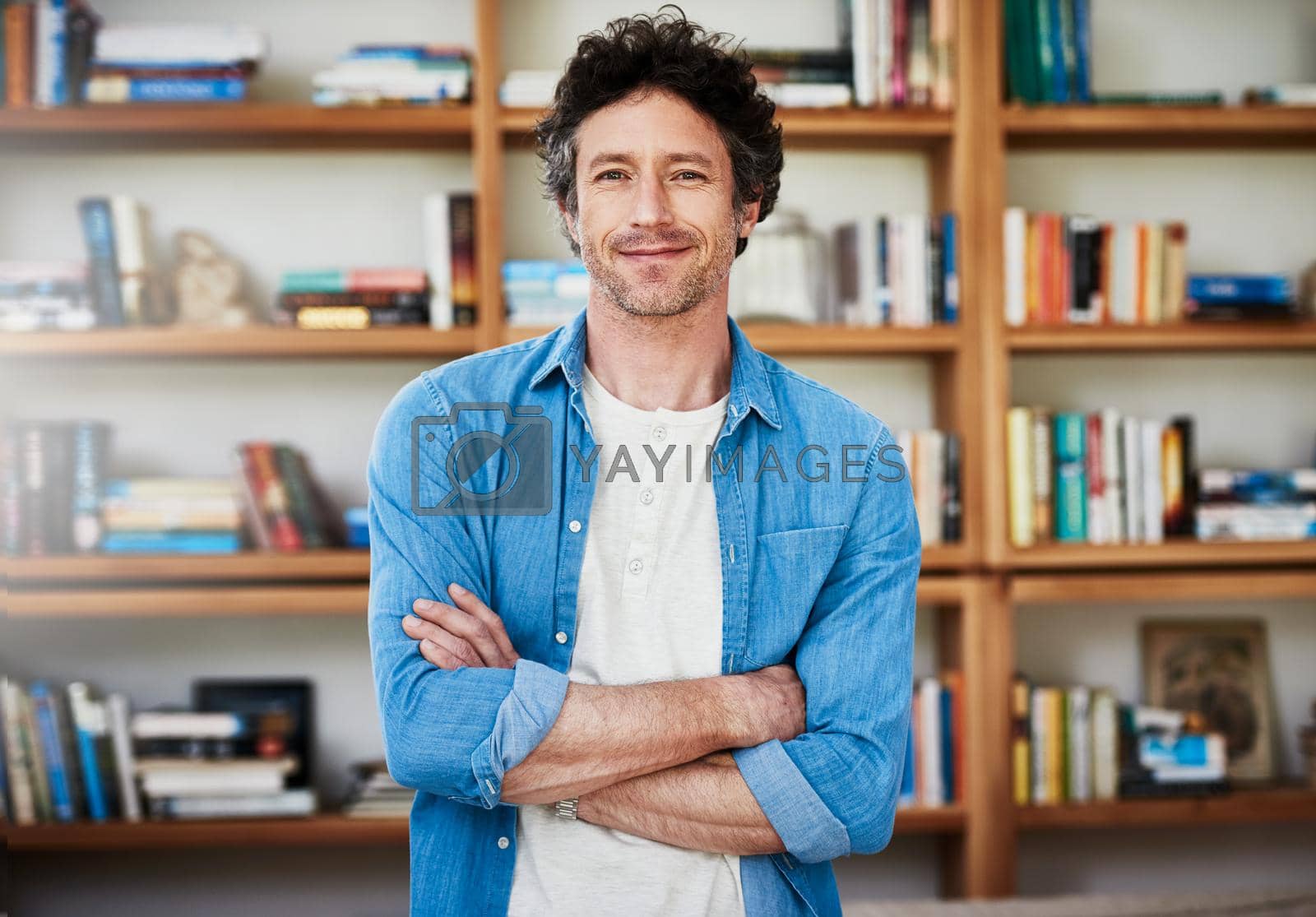 Royalty free image of Hes a self-professed bibliophile. Shot of a happy bachelor posing with his arms crossed in front of a bookshelf at home. by YuriArcurs