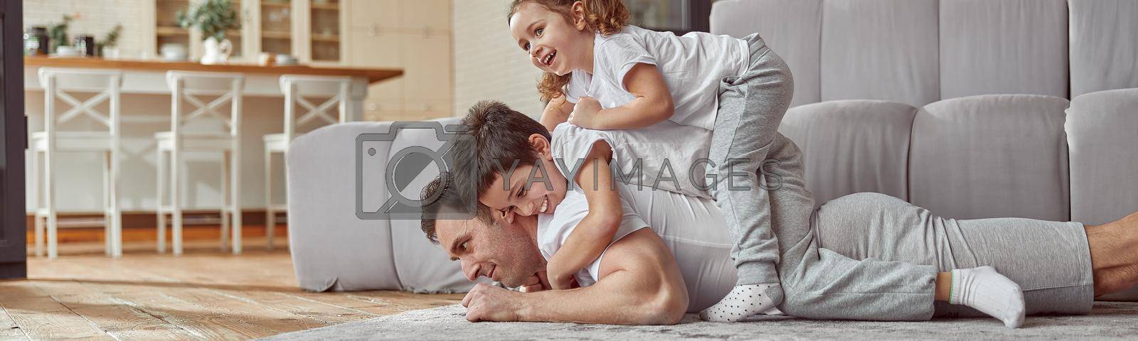 Low angle of jolly son and daughter on dad back while he is lying on floor during training at home