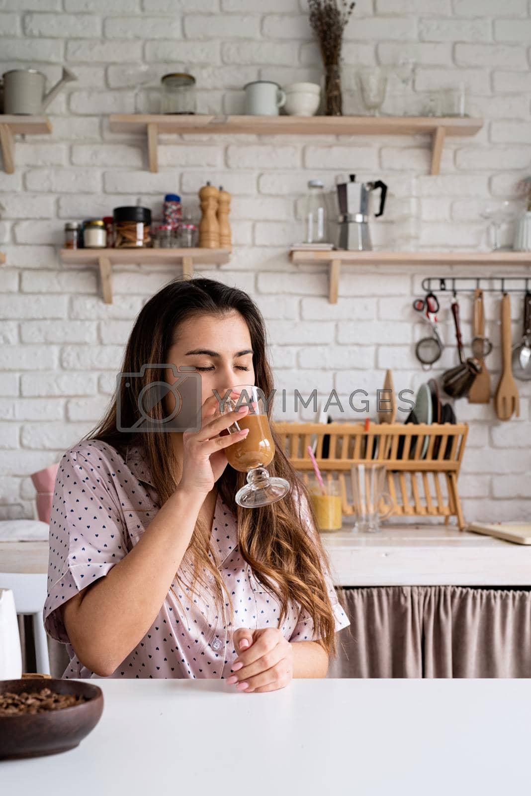 Royalty free image of young woman in lovely pajamas drinking coffee at home kitchen by Desperada