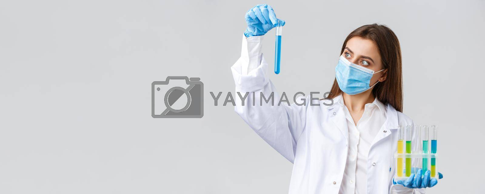 Covid-19, preventing virus, healthcare workers and quarantine concept. Doctor or nurse in clinic lab wear medical mask and gloves, looking at test-tube with coronavirus test vaccine, researching.