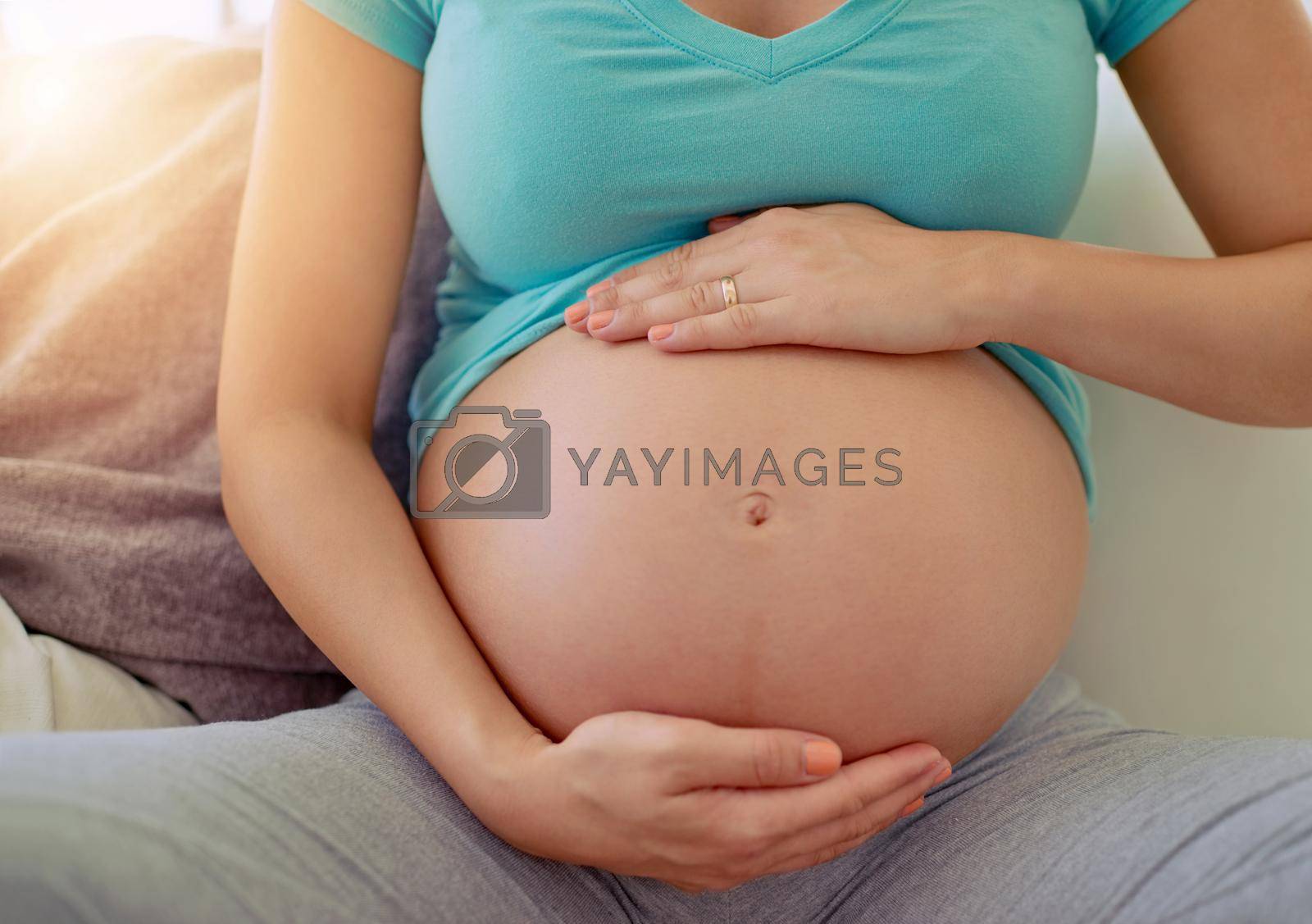 Closeup shot of a pregnant woman holding her belly at home.
