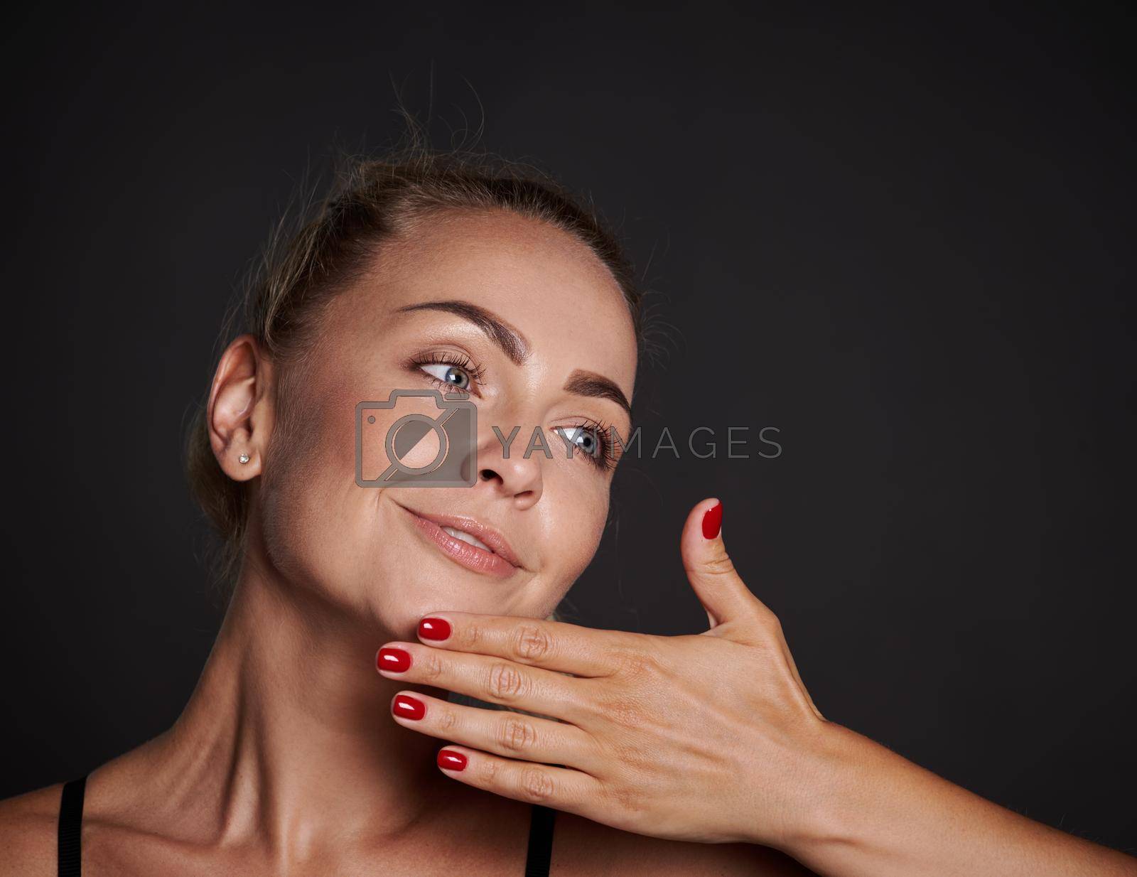 Close-up beauty portrait of a beautiful blonde European woman with clean, radiant tanned skin and well-groomed hands, isolated over black background. Cosmetology, youth concept for ads
