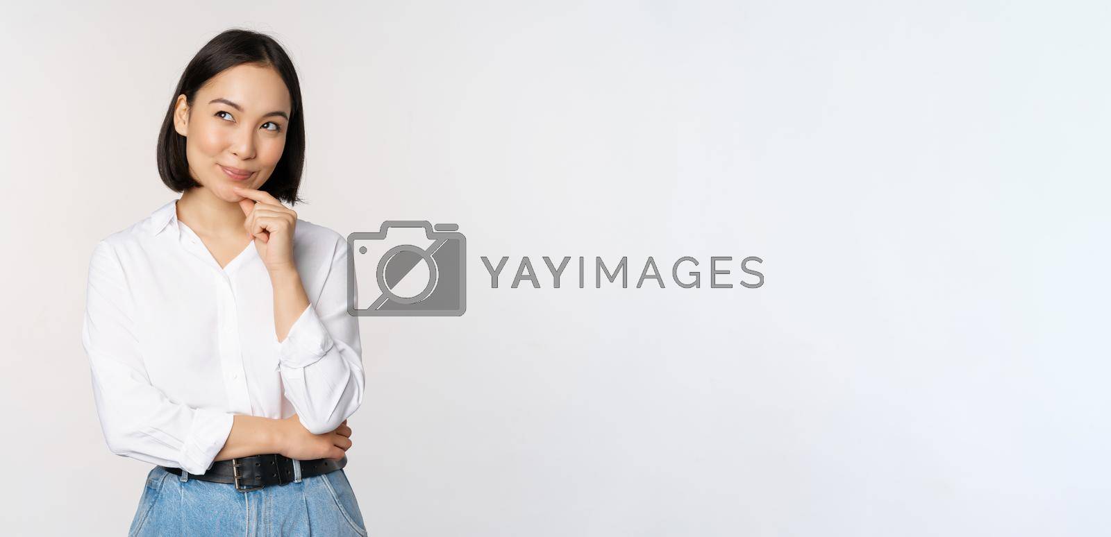 Royalty free image of Image of thoughtful smiling woman has an idea, scheming, planning, looking aside and thinking, standing in office white blouse against studio background by Benzoix