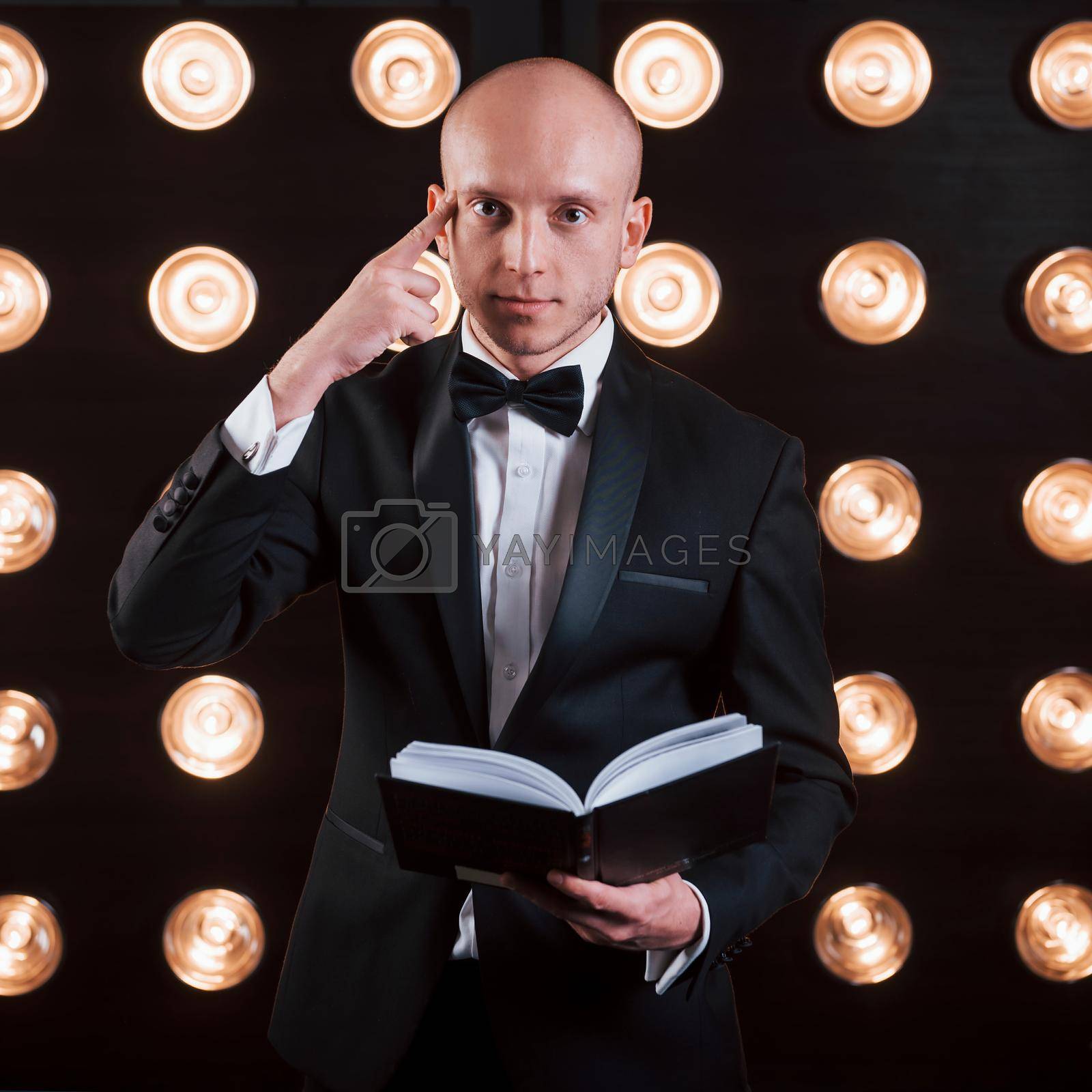 Royalty free image of He know what you thinking about. Magician in black suit standing in the room with special lighting at backstage by Standret
