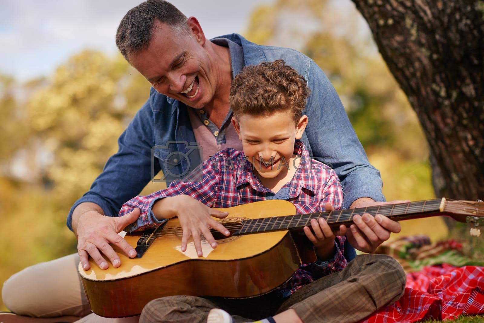 Shot of a father teaching his son how to play guitar while sitting outside.