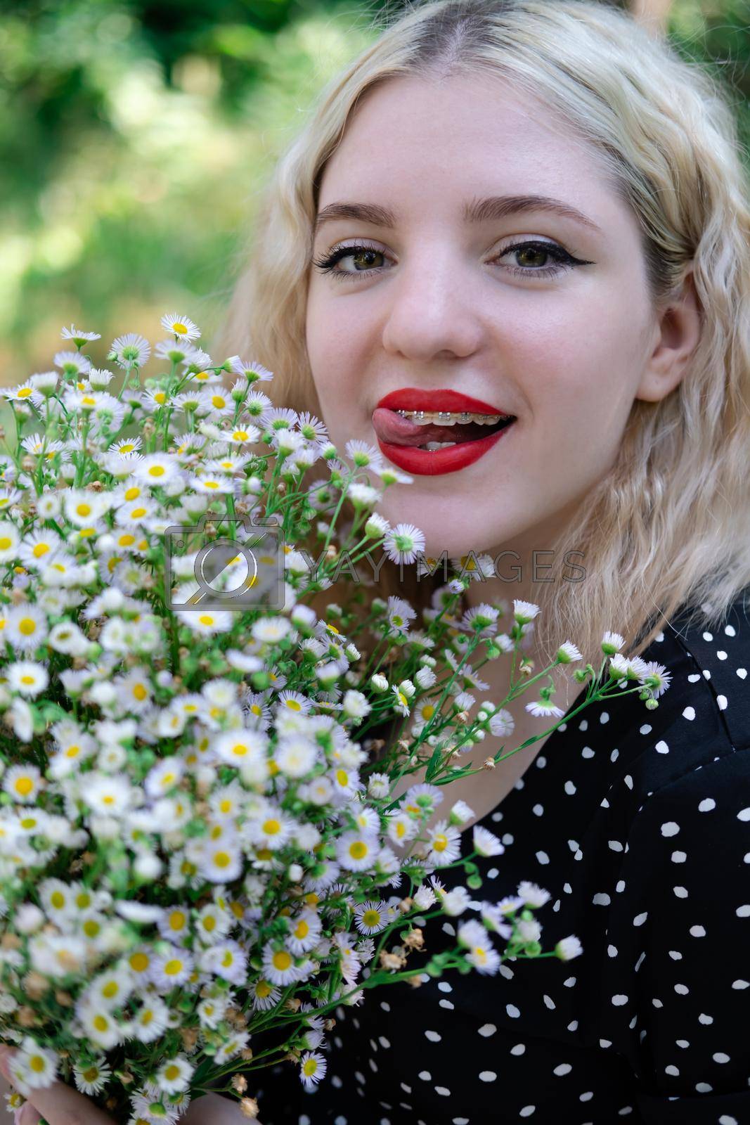portrait of a charming blonde teenage girl wearing teeth braces with bouquet of white wildflowers. female with braces in mouth. healthy teeth. orthodontist dentist.