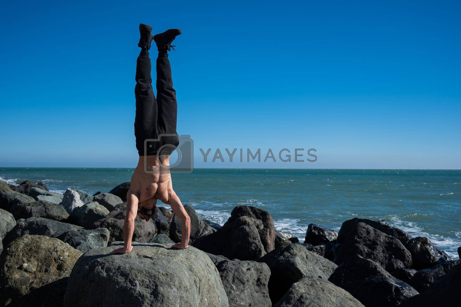 Royalty free image of Shirtless man doing handstand on rocks by the sea. by mrwed54