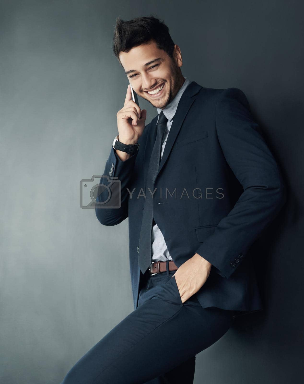 Studio shot of a young businessman talking on a cellphone against a gray background.