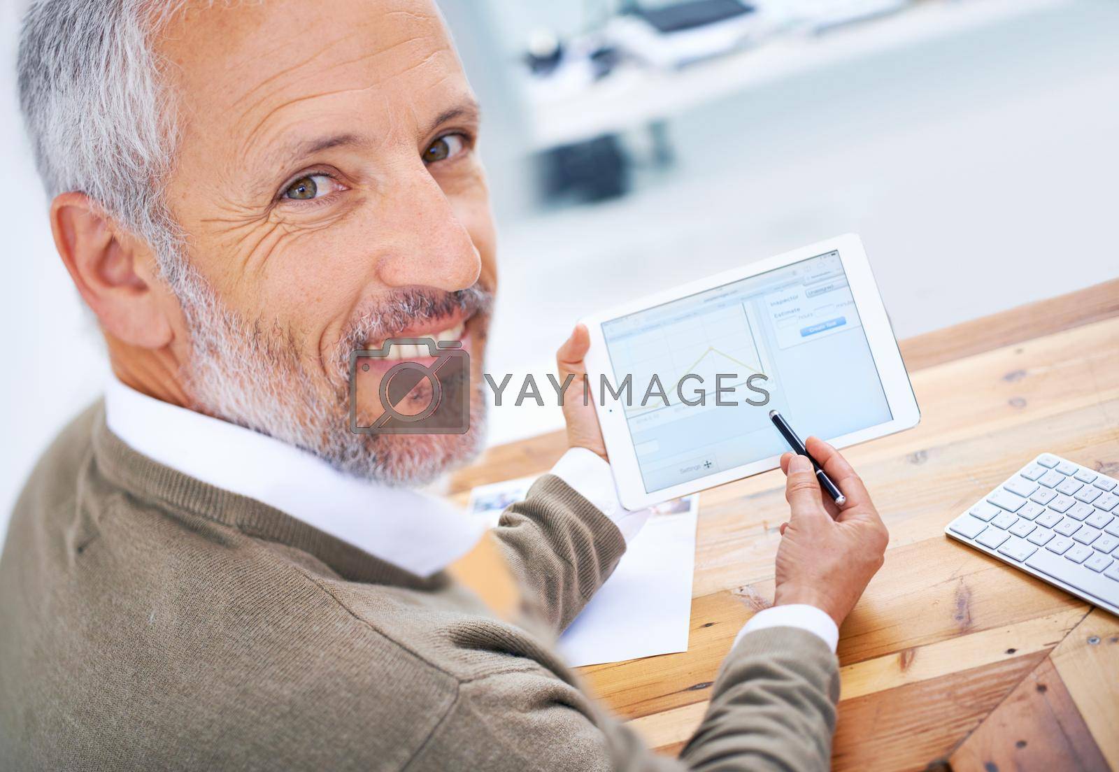 A portrait of a happy businessman using a tablet at his desk.