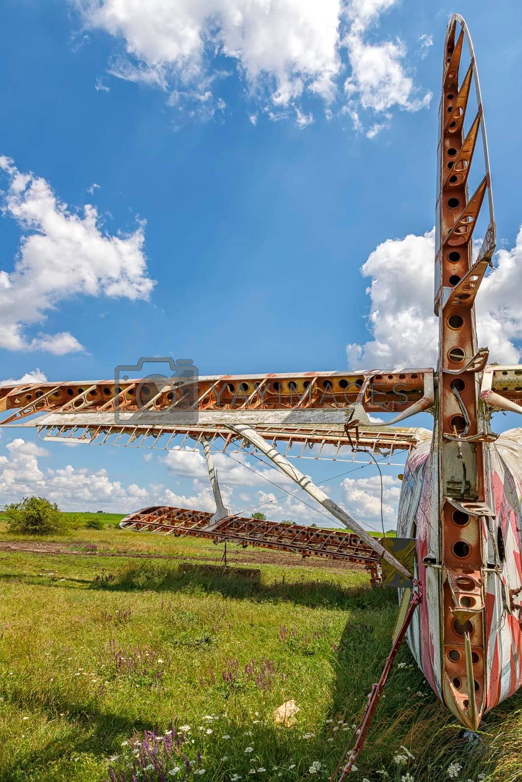 a part of abandoned aircraft plane standing in the field against the cloudy blue sky.