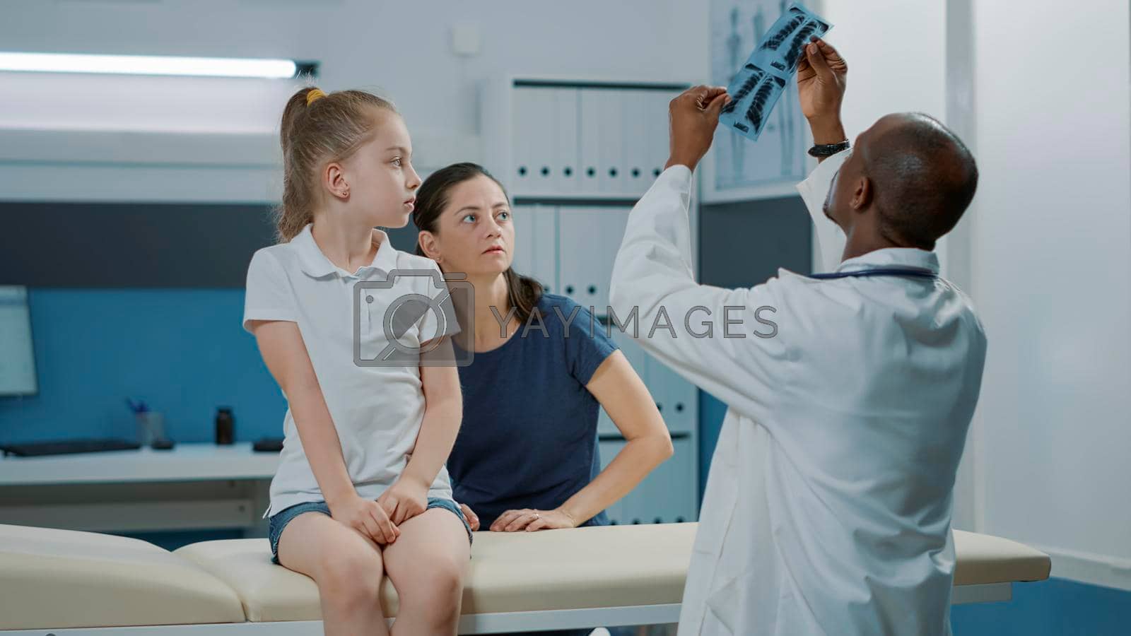 Pediatrician showing radiography results to mother and child at medical appointment. Physician explaining x ray scan diagnosis to small patient and adult in cabinet at checkup examination.
