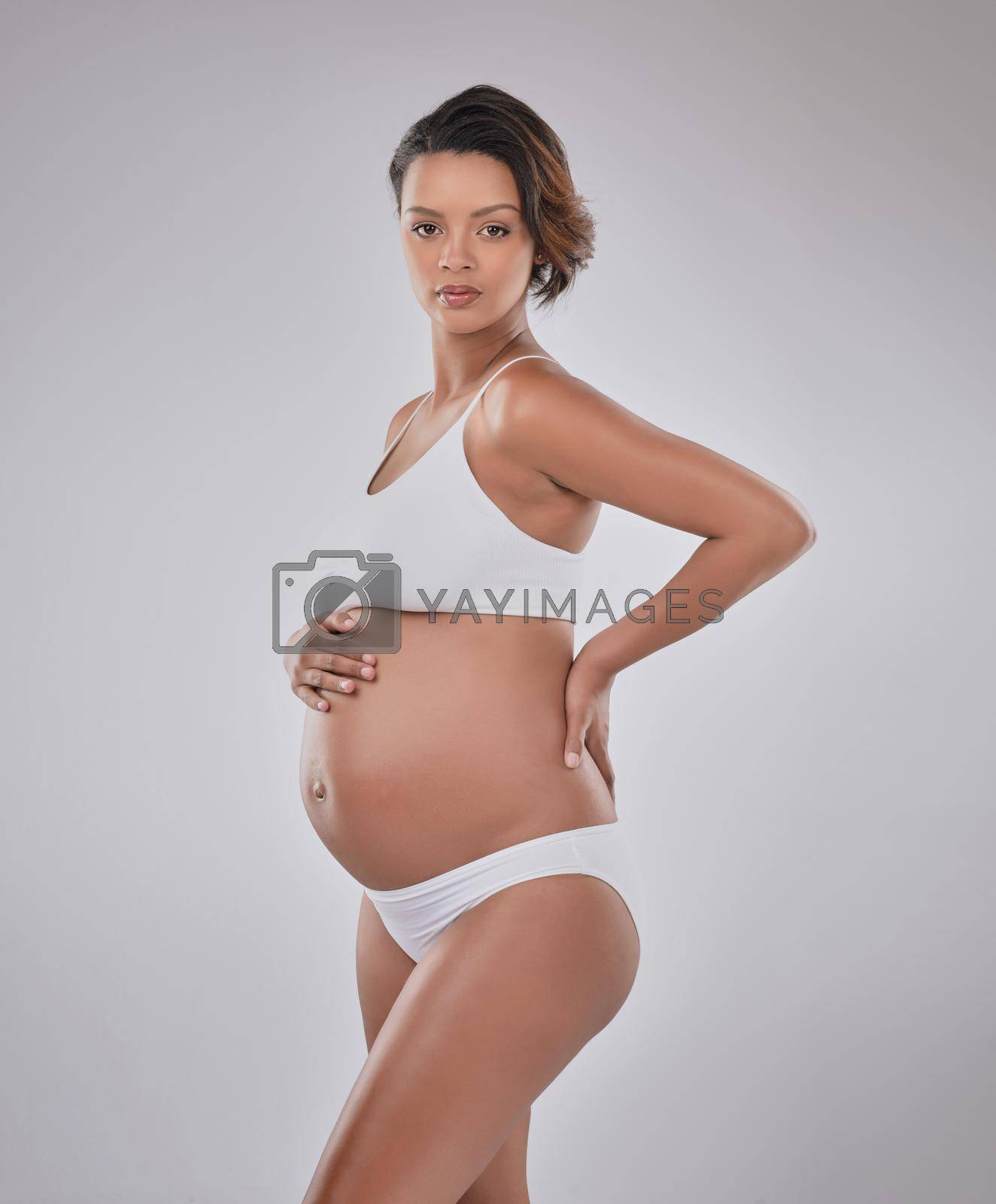 Studio portrait of a beautiful young pregnant woman posing against a gray background.
