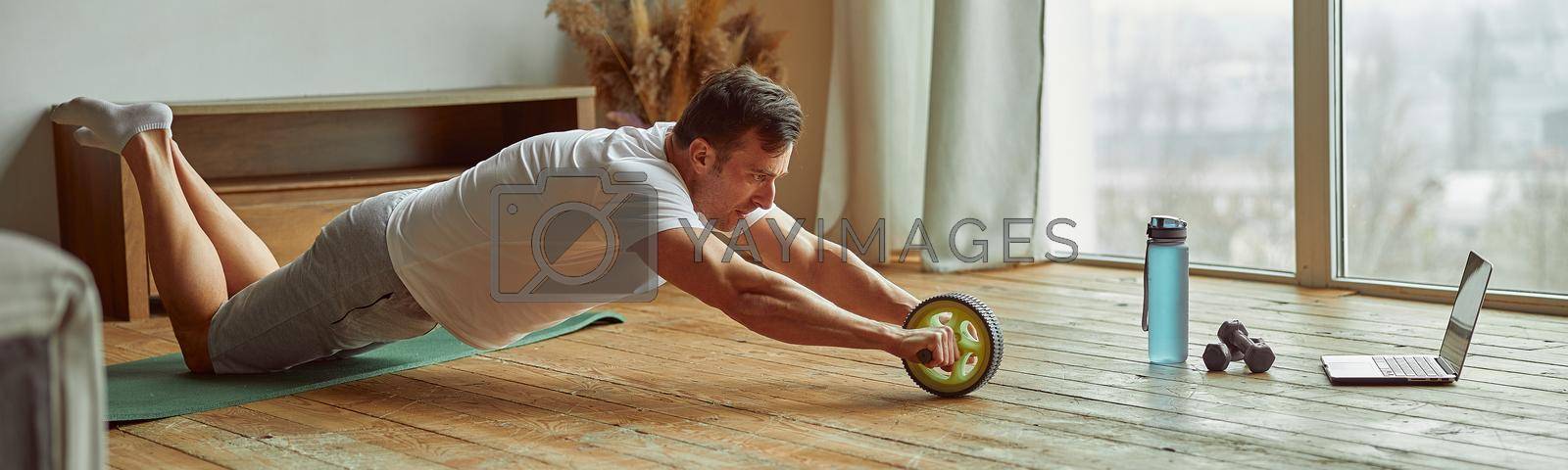 Royalty free image of Man doing training with equipment and laptop indoors by Yaroslav_astakhov