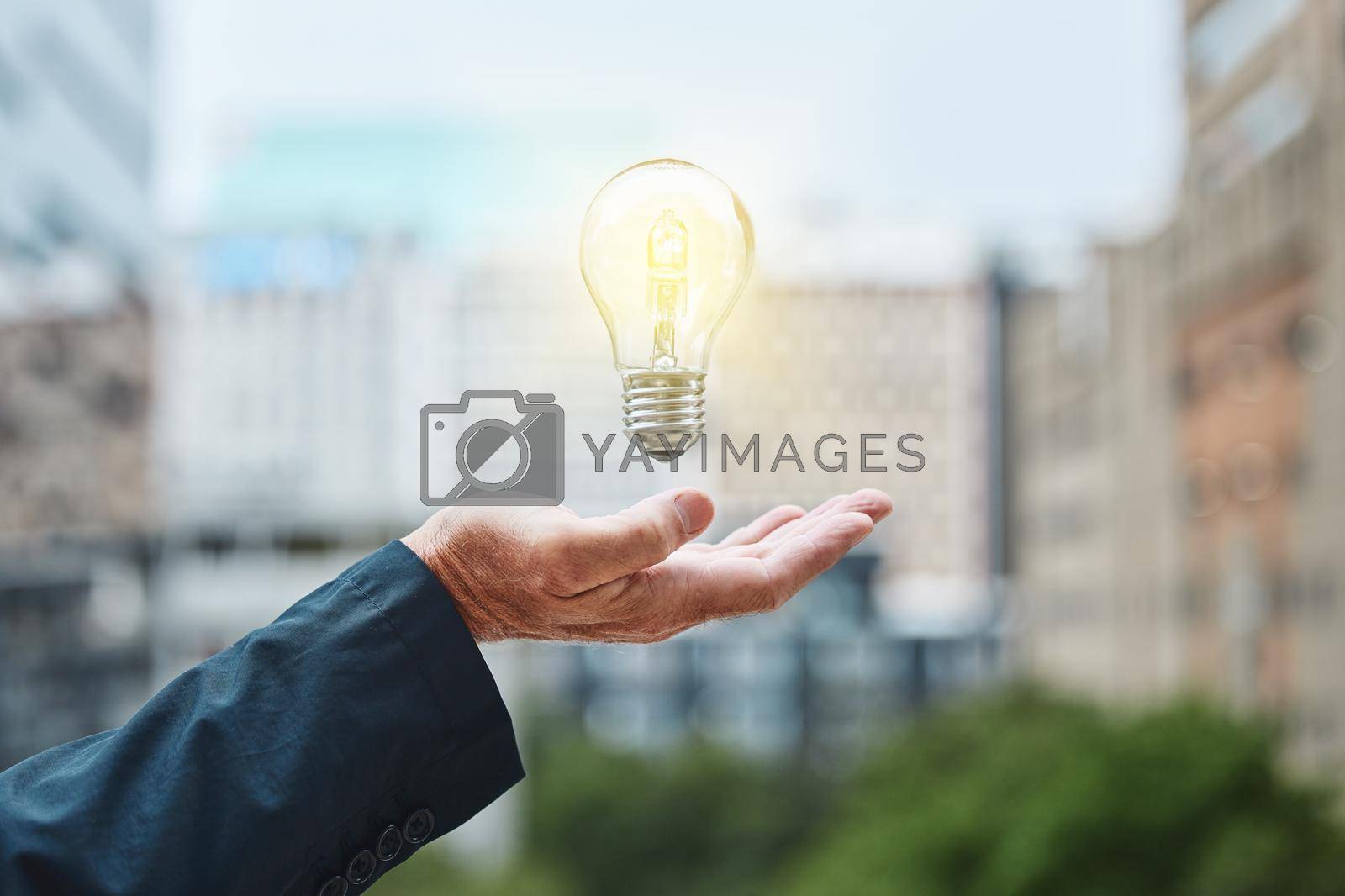 Shot of an unrecognisable businessman holding a lightbulb against an urban background.