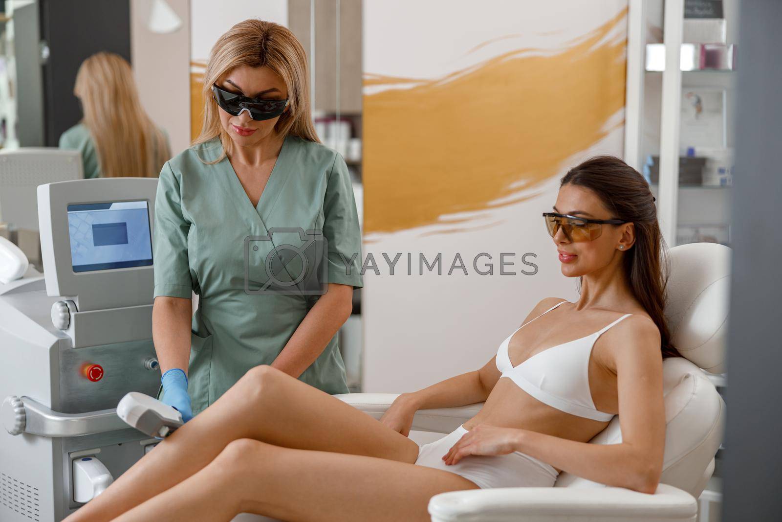 Hair removal procedure on legs in beauty salon, two women. Photo epilation concept