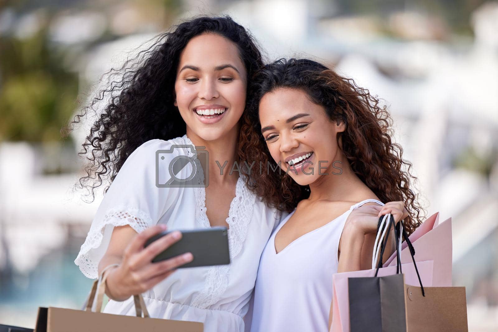 Shot of two young women taking selfies while shopping against an urban background.